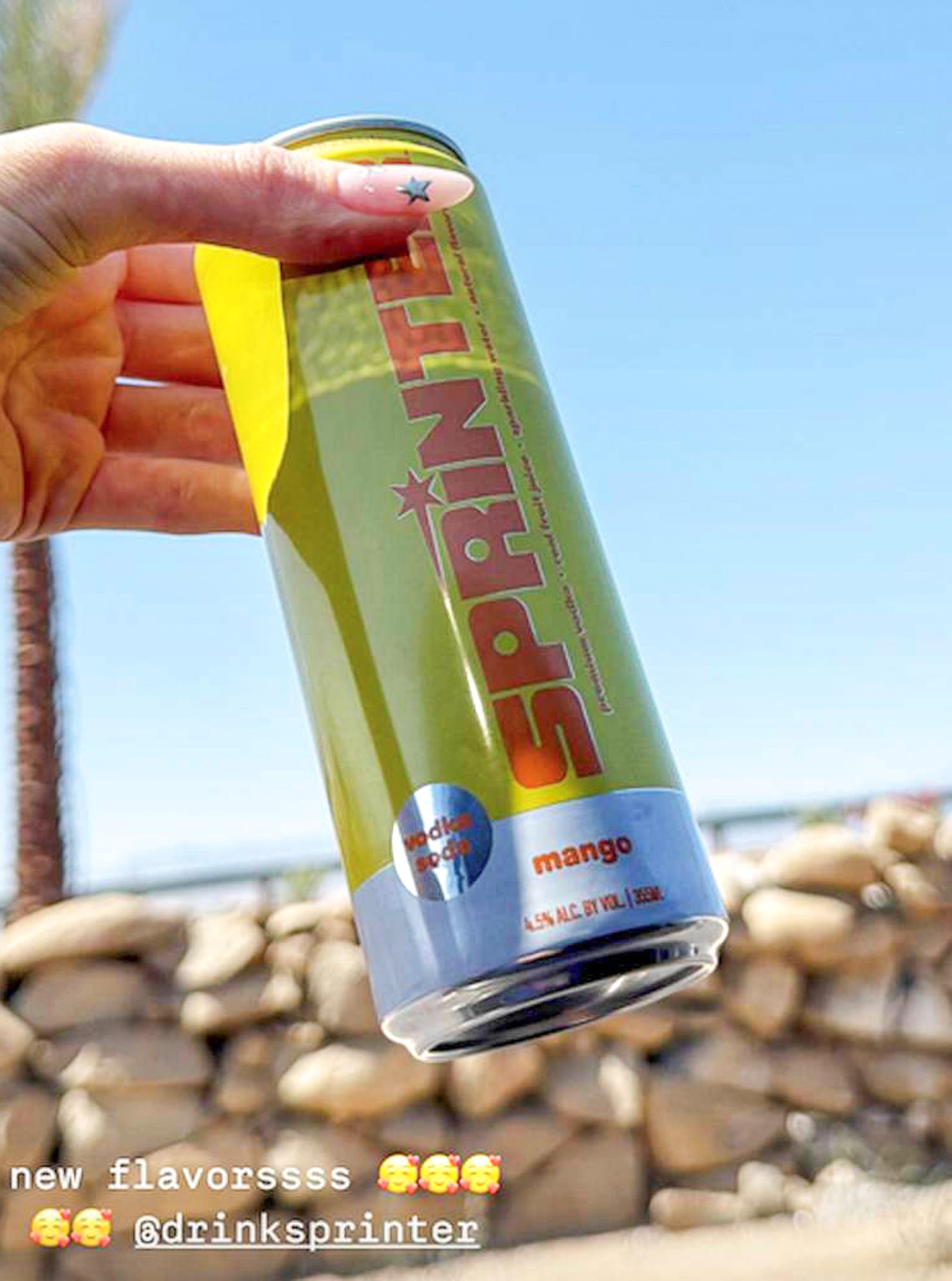 Eine Hand hält eine gelbe Sprinter-Dose mit der Geschmacksrichtung Mango vor einem sonnigen, blauem Himmel.