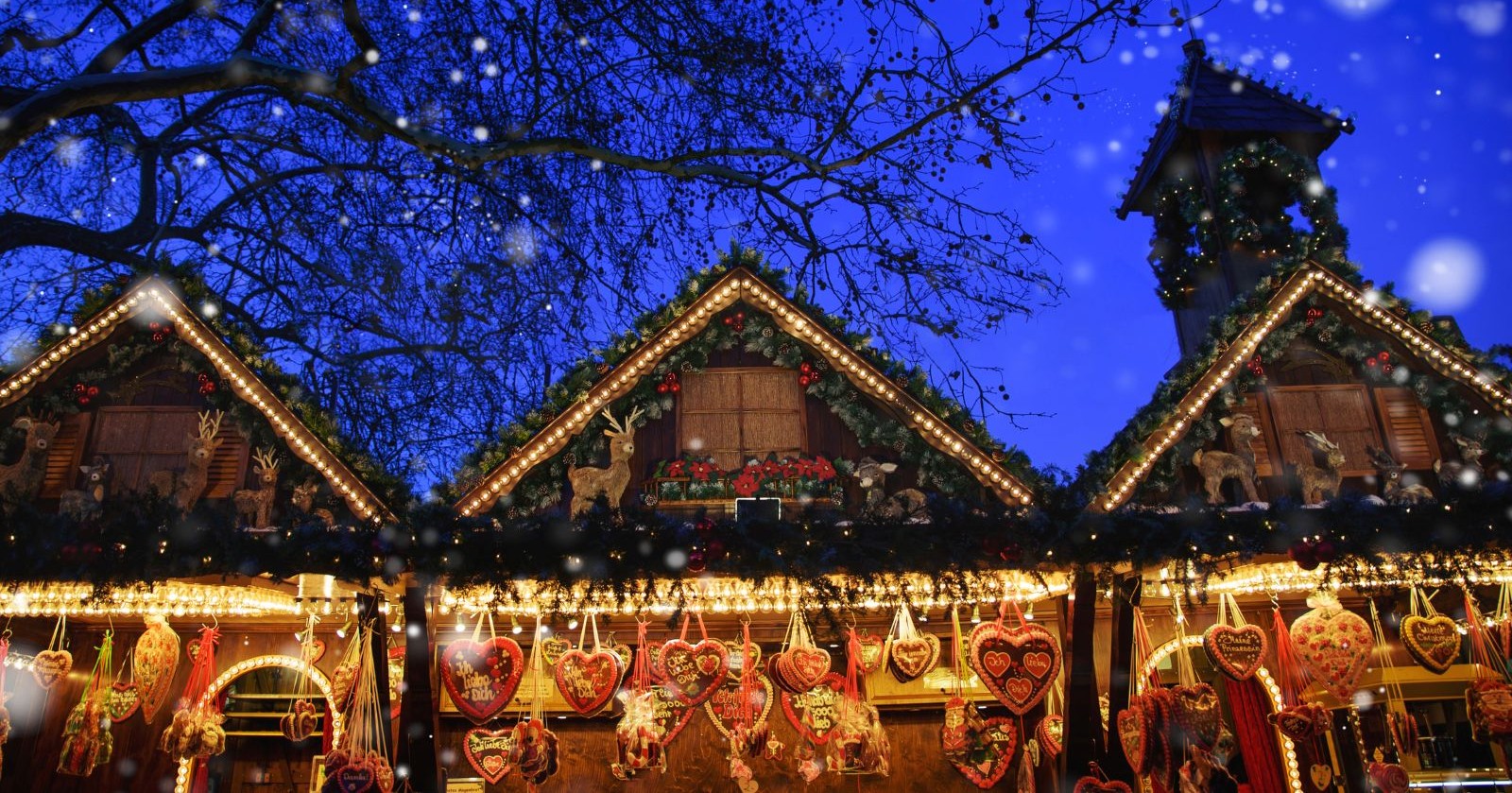 Beleuchtete Weihnachtsmarktstände mit Lebkuchenherzen und Weihnachtsdekoration am Abend, Symbolbild für die Diskussion um Bargeld- und Kartenzahlung auf Märkten.