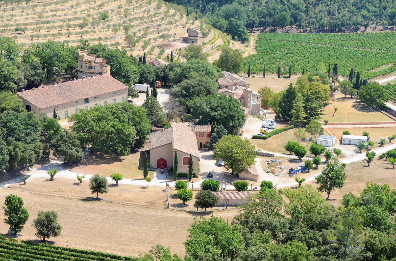 Luftaufnahme eines weitläufigen Weinguts mit mediterranen Gebäuden, Weinreben, Olivenhainen und umliegenden Hügeln.