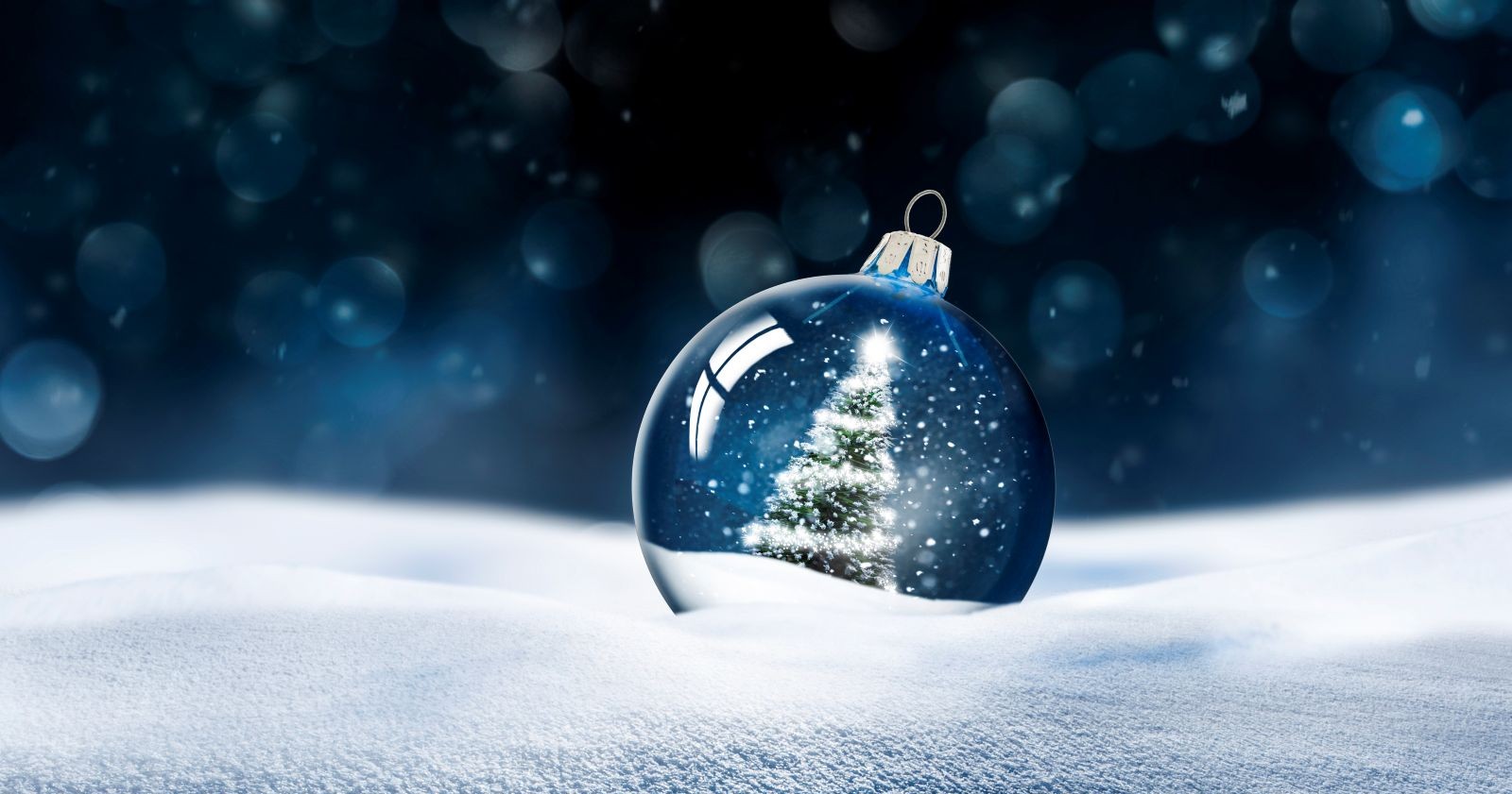 Transparente Schneekugel mit einem Tannenbaum, der weihnachtlich geschmückt ist in einer verschneiten Landschaft