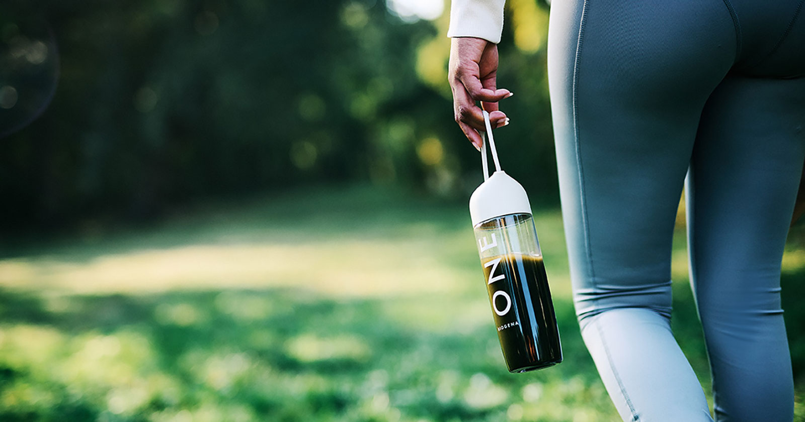Junge Frau geht mit Trinkflasche in der Hand durch die Natur | Credit: BIOGENA