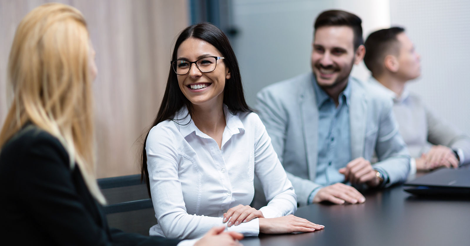 Junge Frauen und Männer bei einem Meeting um einen Tisch versammelt | Credit: Trainingday