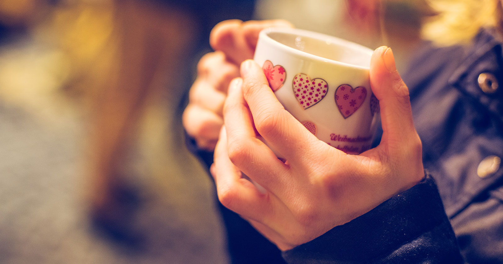 Frau beim Weihnachtsmarkt mit Punsch-Becher in der Hand | Credit: iStock.com/Patrick Daxenbichler