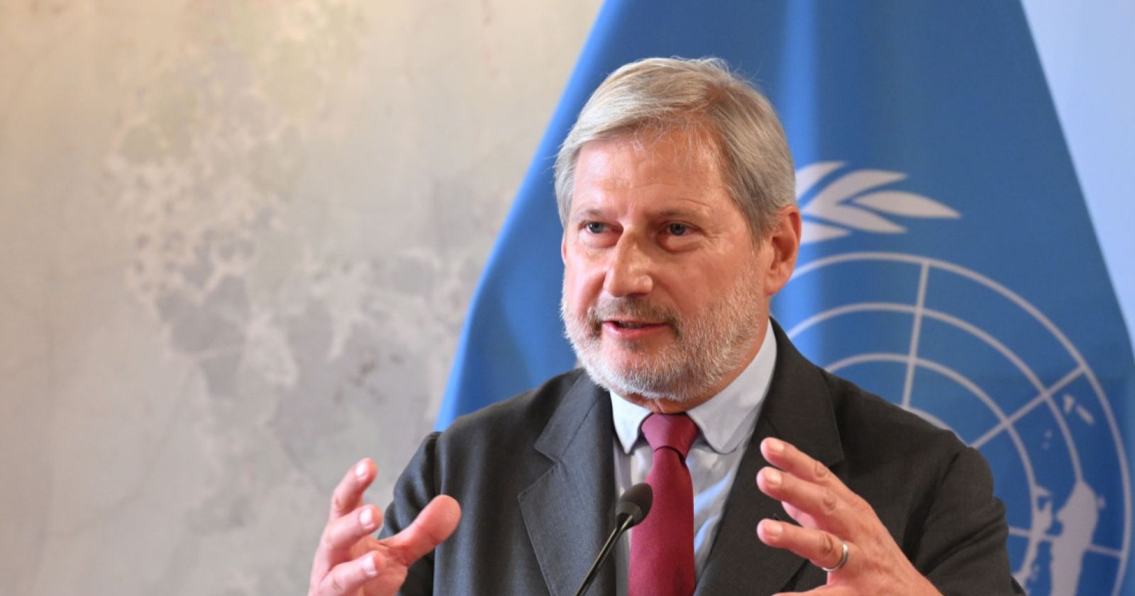 Johannes Hahn spricht bei einer Pressekonferenz vor einer blauen Flagge mit Weltkarten-Symbol, er wird neuer Präsident des OeNB-Generalrats.