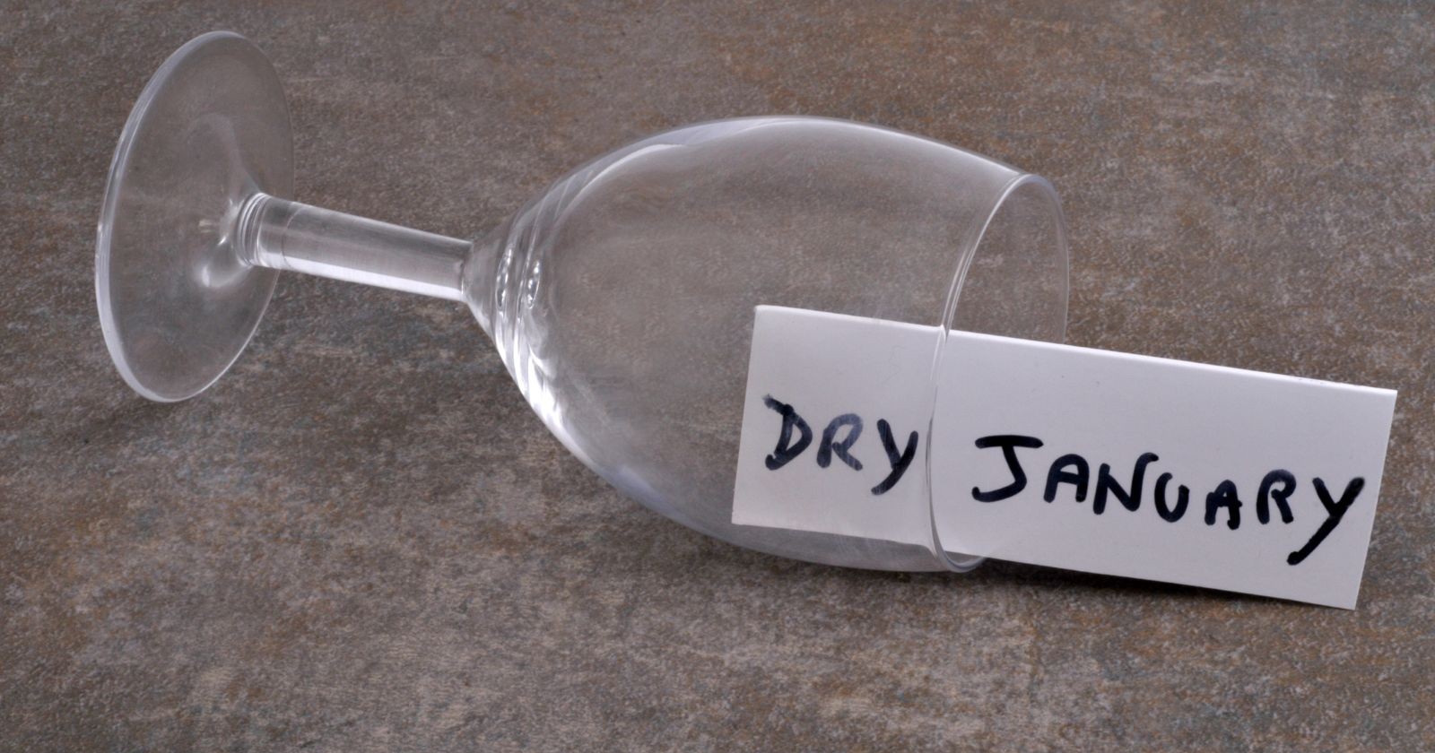 Leeres, umgestoßenes Weinglas, in dem auf einem Zettel Dry January geschrieben steht