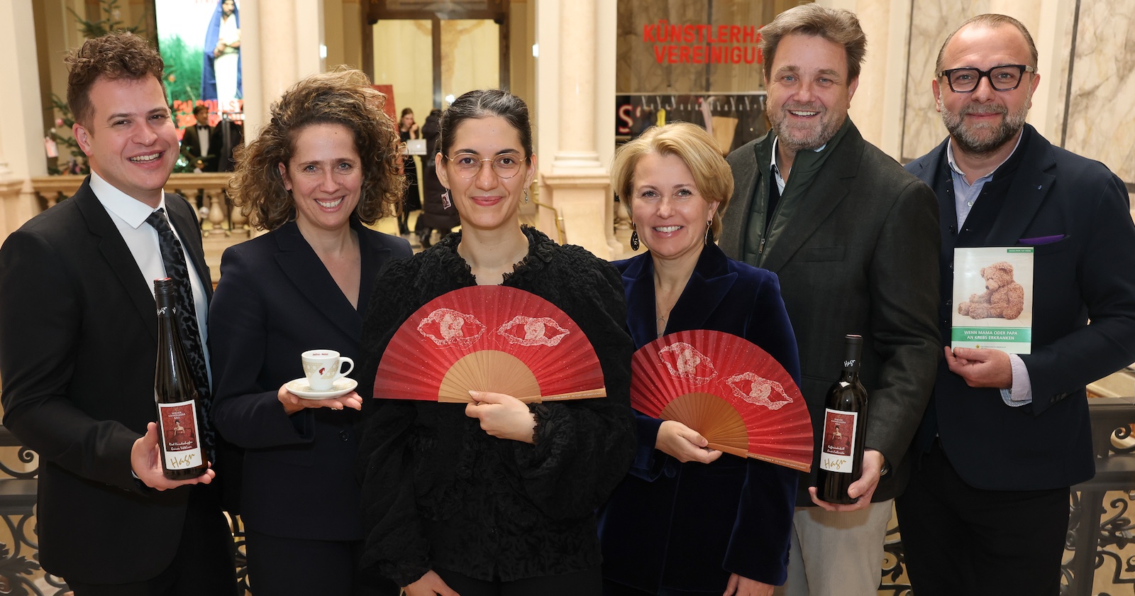 Sechs Personen in schwarzer Kleidung präsentieren den neuen Ballfächer und den Wein zum Kaffeesiederball 2026