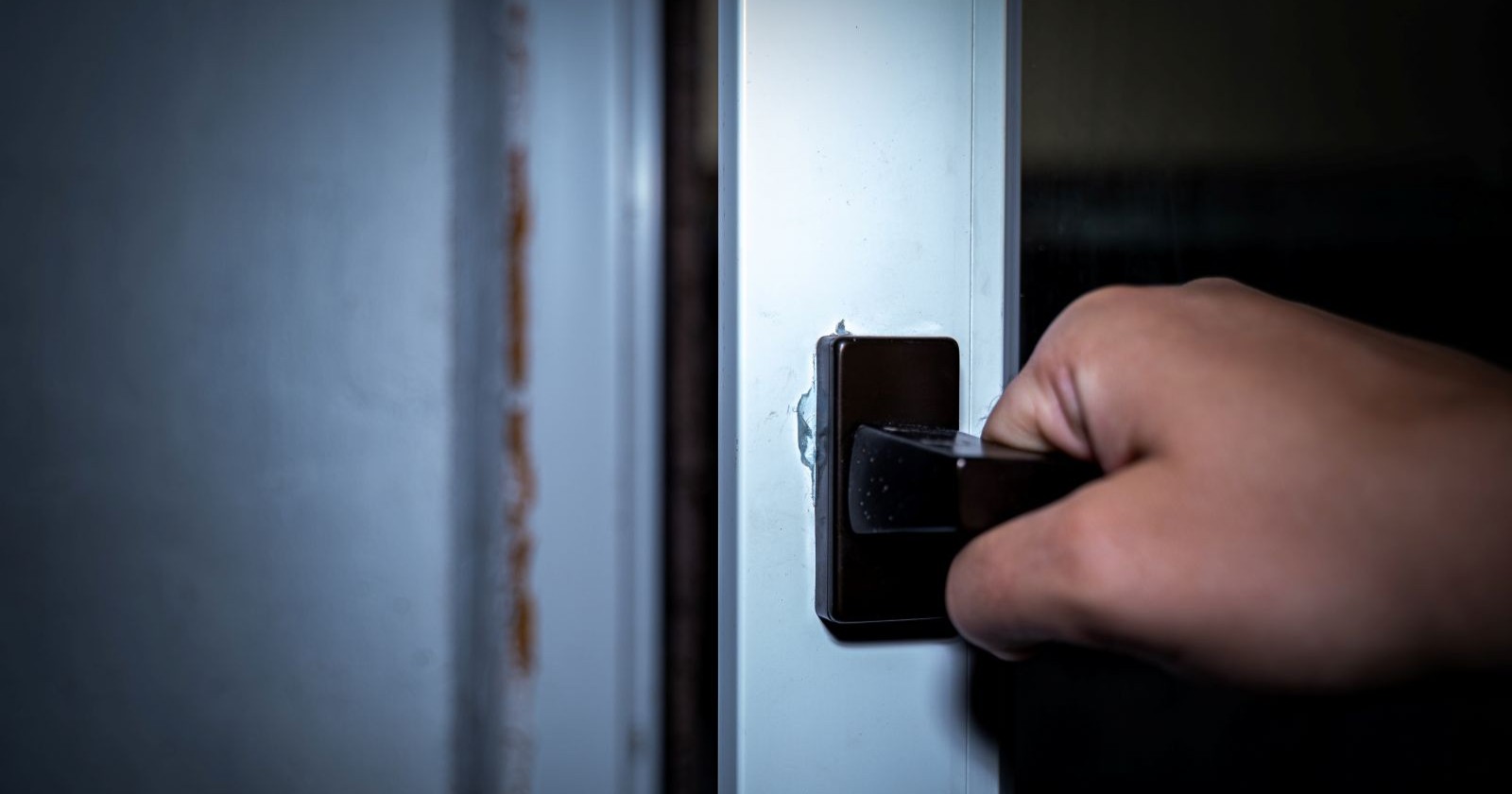 Männerhand öffnet die Tür eines Fensters in der Dunkelheit