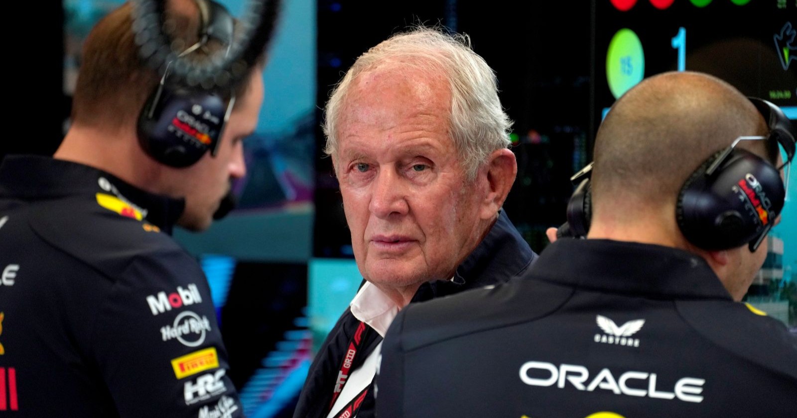 Helmut Marko im Red-Bull-Teambereich zwischen zwei Teammitgliedern mit Headsets, mit ernster Miene in die Kamera blickend, aufgenommen während des Formel-1-Wochenendes in Katar.
