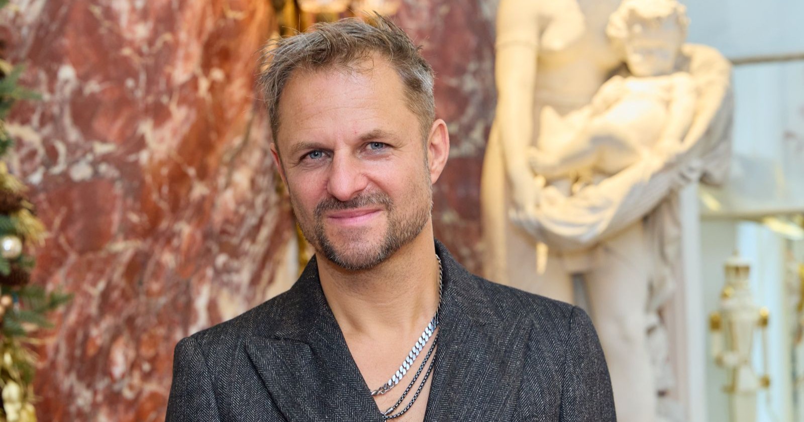 Philipp Hochmair lächelt vor Marmorwand