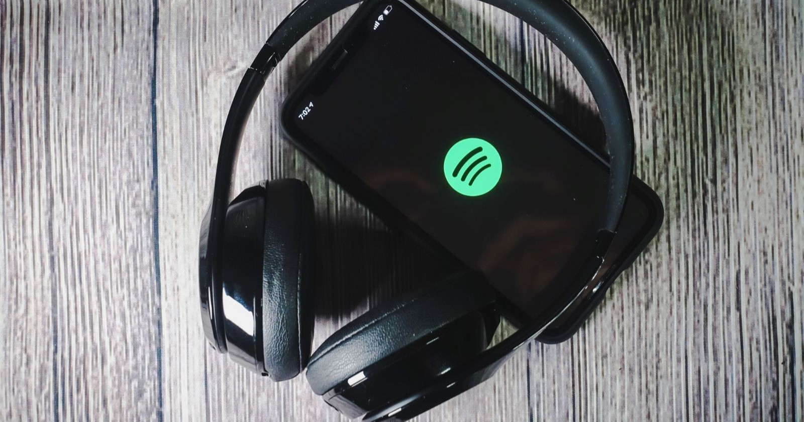 Kopfhörer auf einer grauen Holzoberfläche um ein iPhone auf dem das App-Icon von Spotify angezeigt wird
