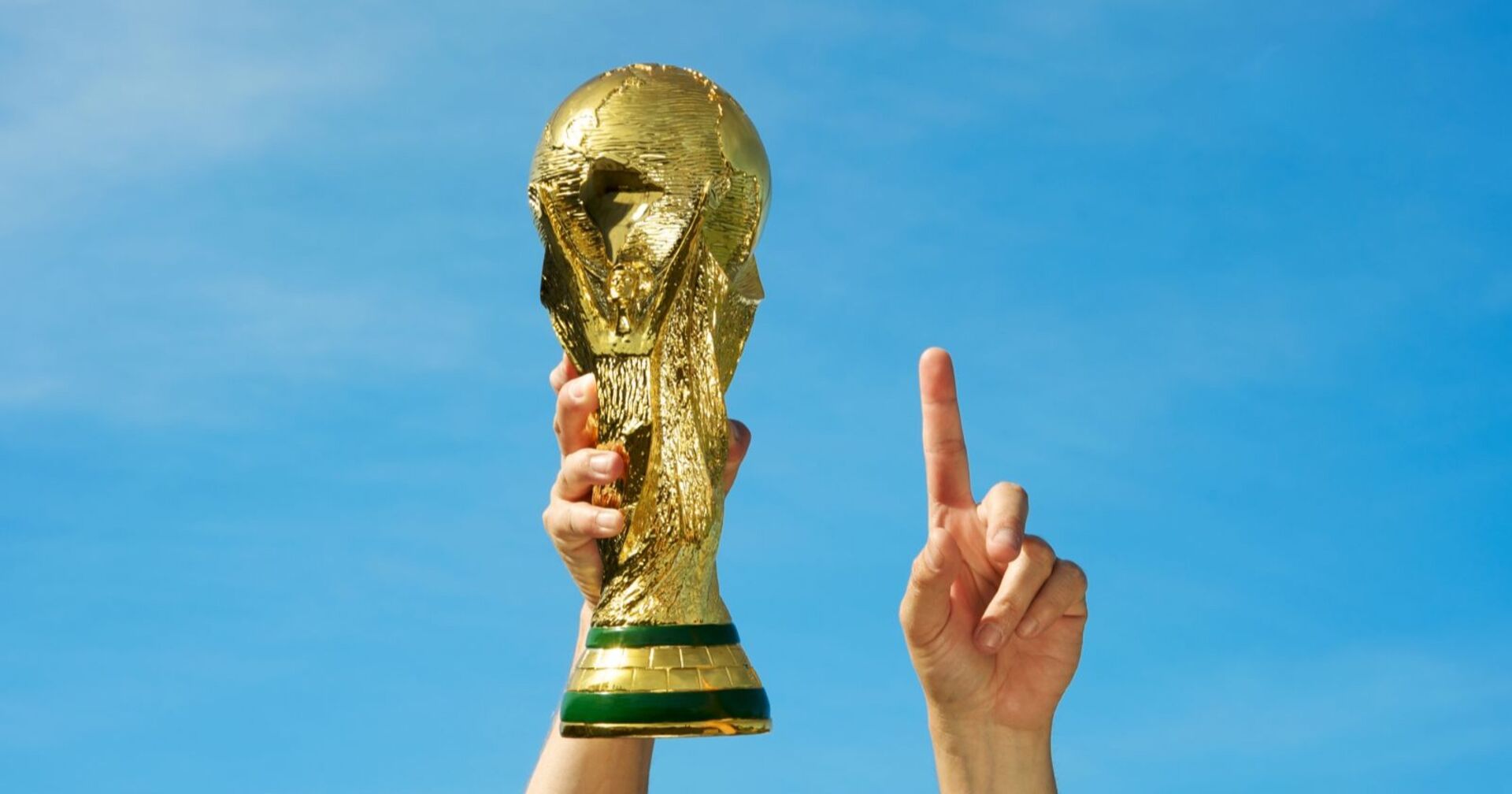 Mensch, der in seiner linken Hand WM-Pokal hält und seinen rechten Zeigefinger nach oben streckt