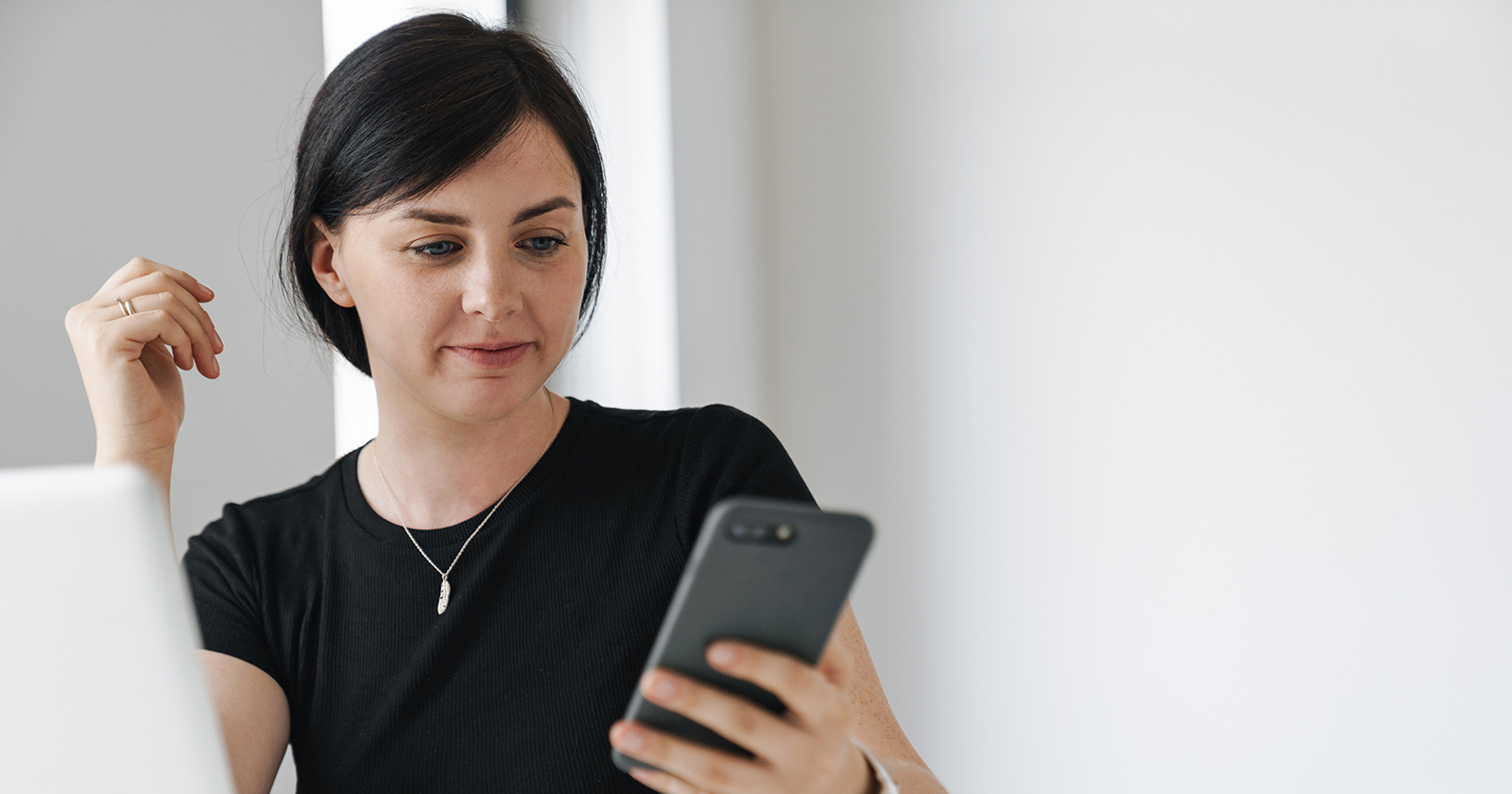 Frau mit Smartphone vor dem Notebook | Credit: Adobe Stock/Drobot Dean