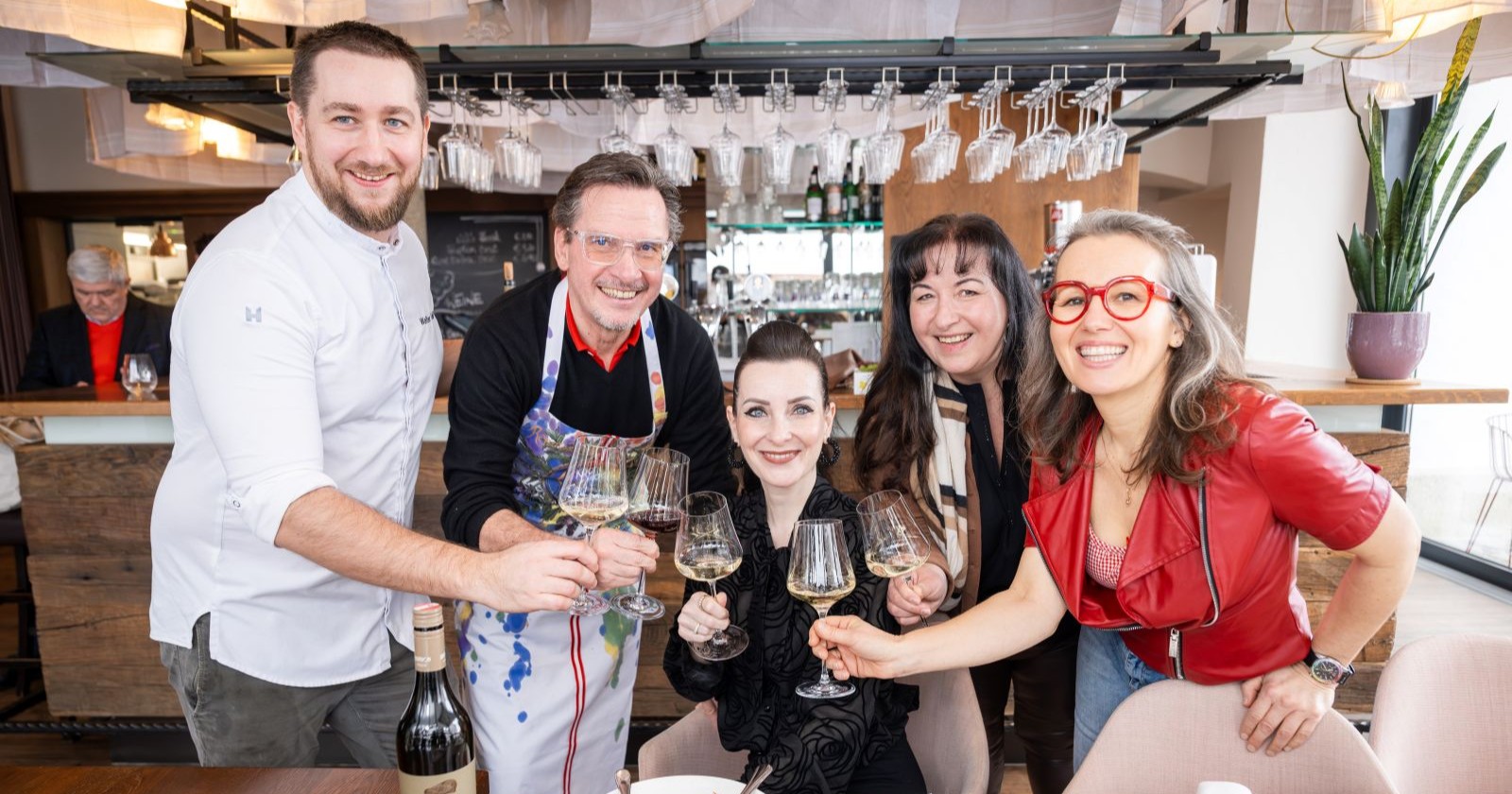 Zwei Männer und drei Frauen stoßen mit einem Glas Wein an