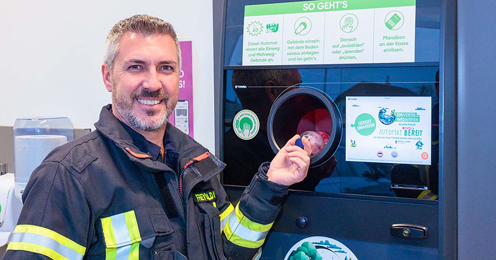 Ein Mann in Feuerwehruniform, der Leergut in einen Pfandrücknahmeautomaten einwirft.