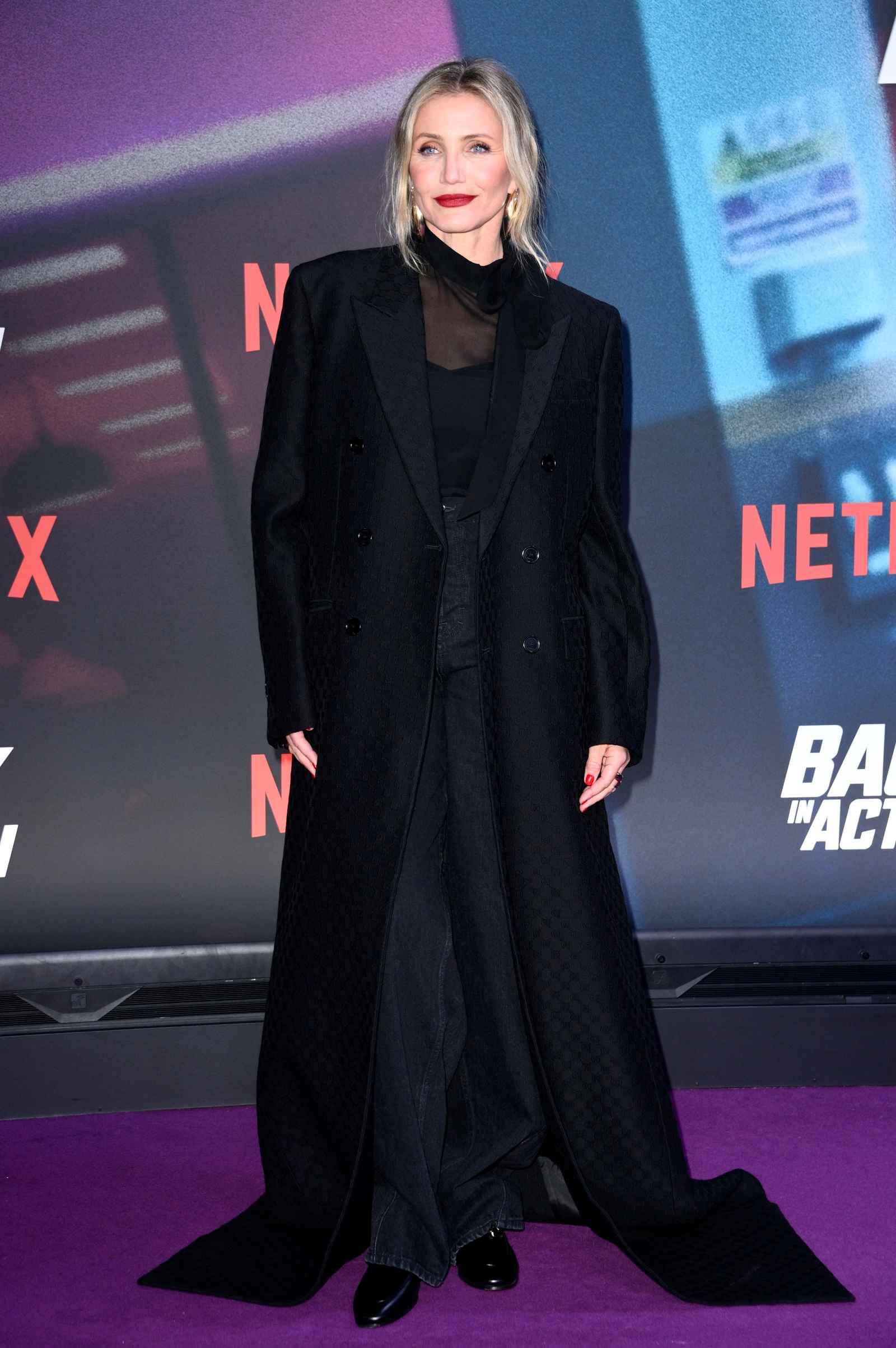 Cameron Diaz posiert auf dem roten Teppich vor einer Netflix-Fotowand in einem langen schwarzen Mantel.