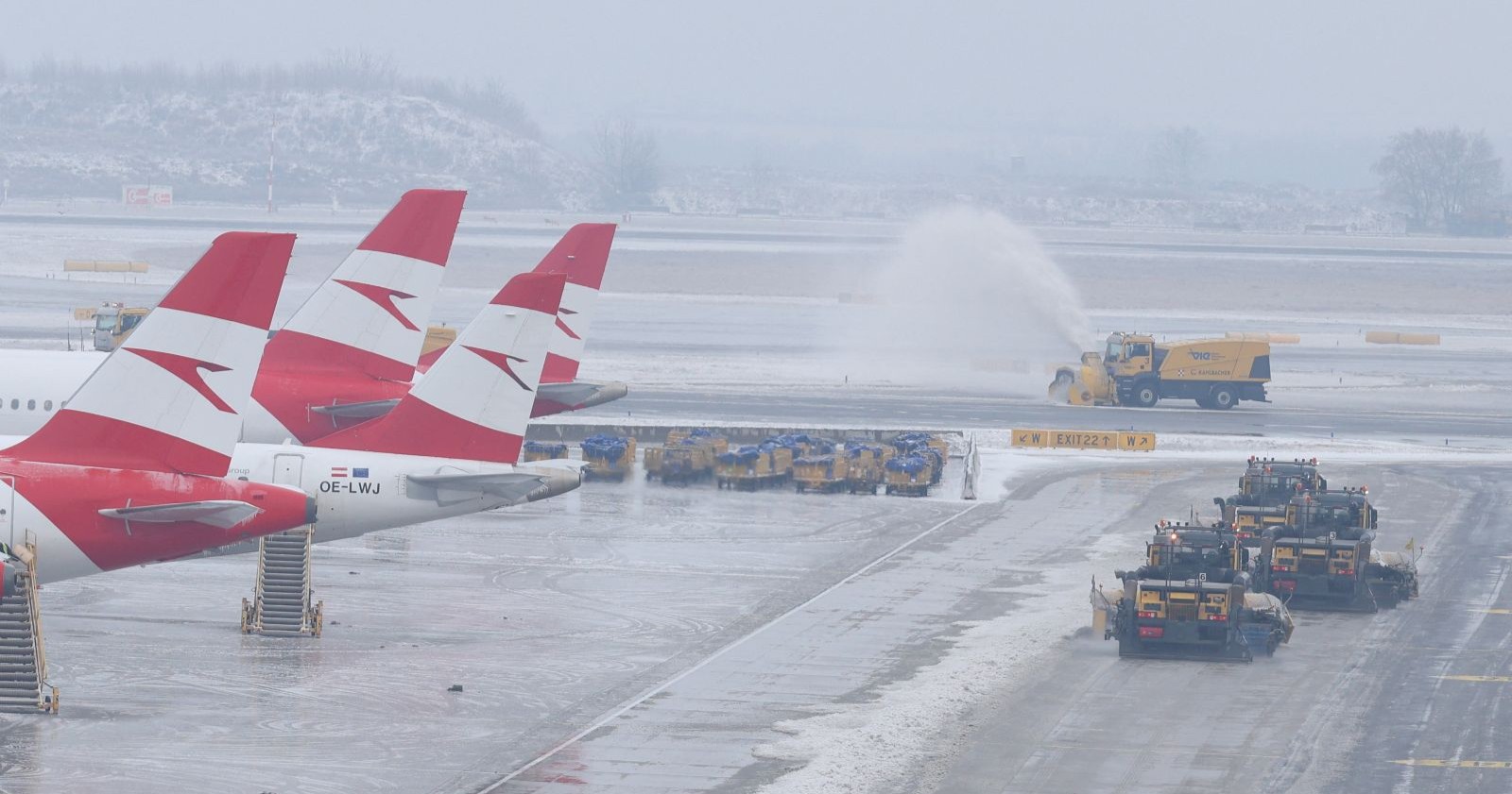Winterdienstfahrzeuge räumen vereiste Pisten am Flughafen Wien-Schwechat, mehrere Austrian-Airlines-Flugzeuge stehen still; deutliche Auswirkungen des Glatteischaos auf den Flugbetrieb.