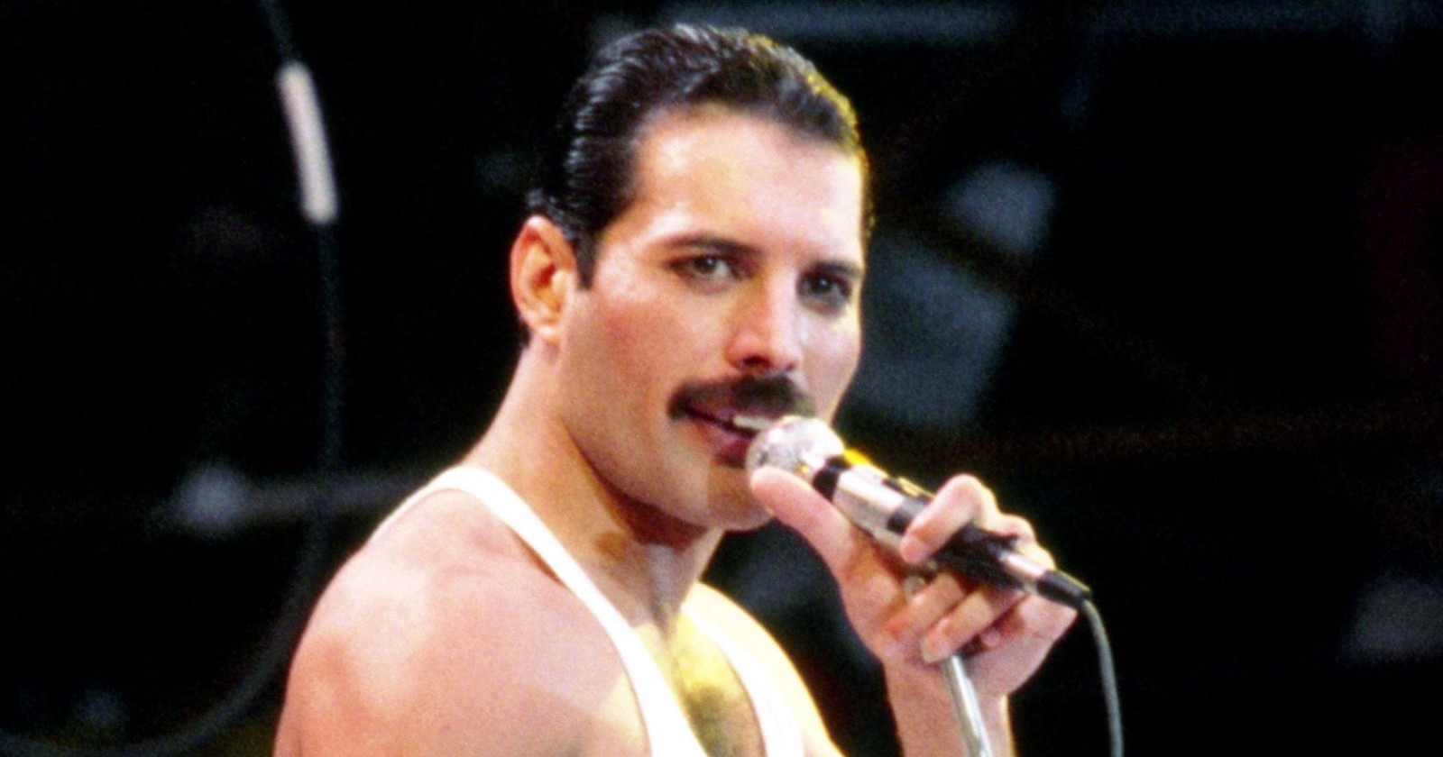 Freddie Mercury singt auf der Bühne in einem weißen Outfit und hält ein Mikrofon, gefangen in einem intensiven Moment seiner Performance.