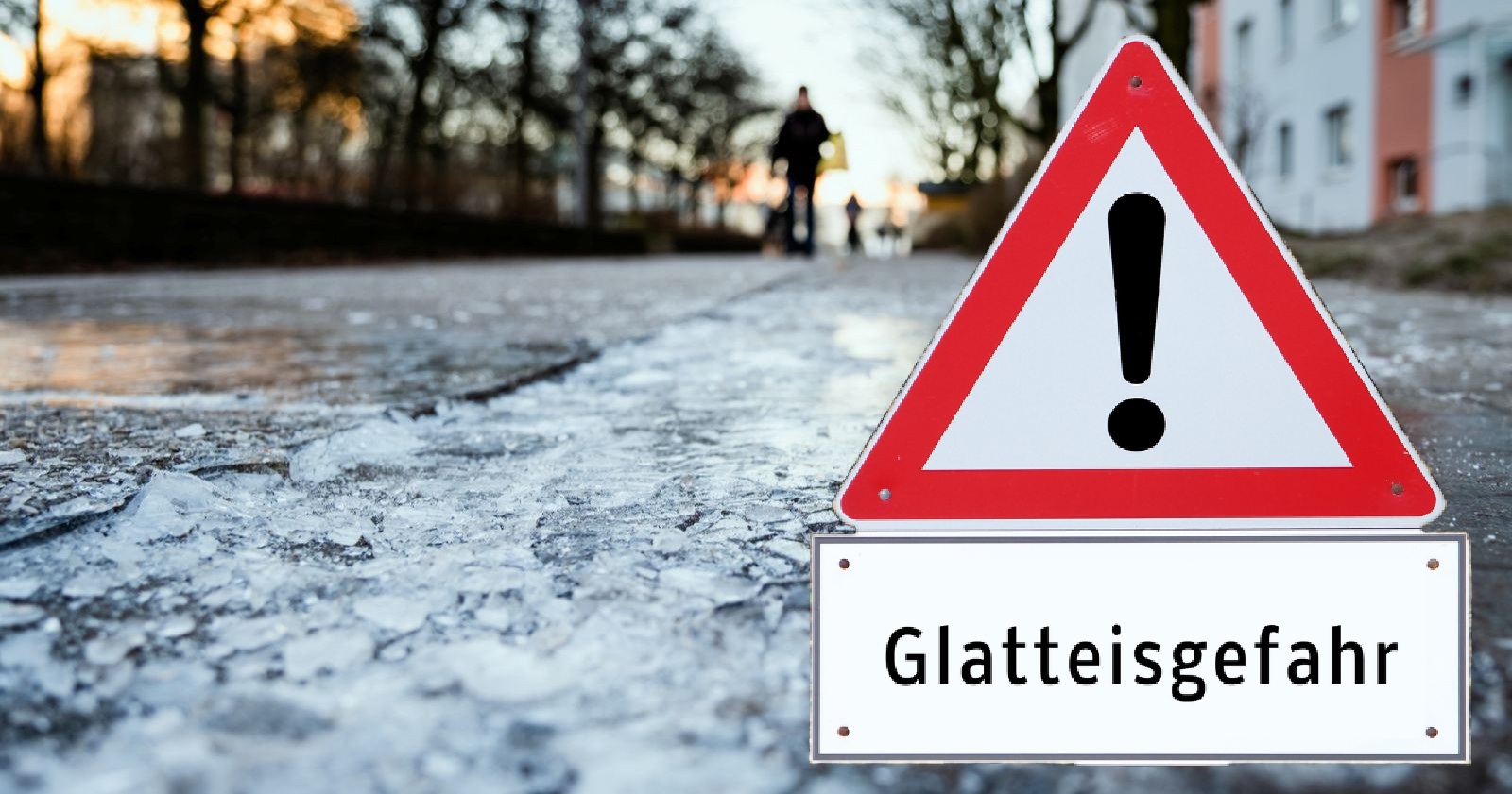 Verkehrswarnschild auf vereister Straße mit deutlicher Glatteisgefahr; glatte Oberfläche und Eisplatten zeigen das erhöhte Risiko durch aktuelle Glatteiswarnung.