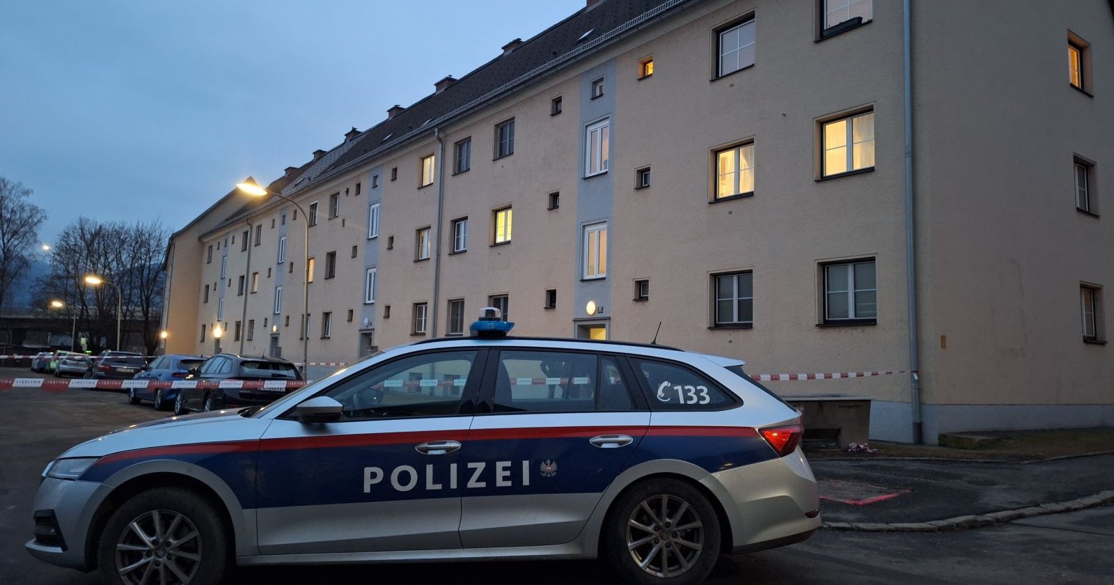Ein Polizeiauto steht vor einem beleuchteten Wohnhaus.