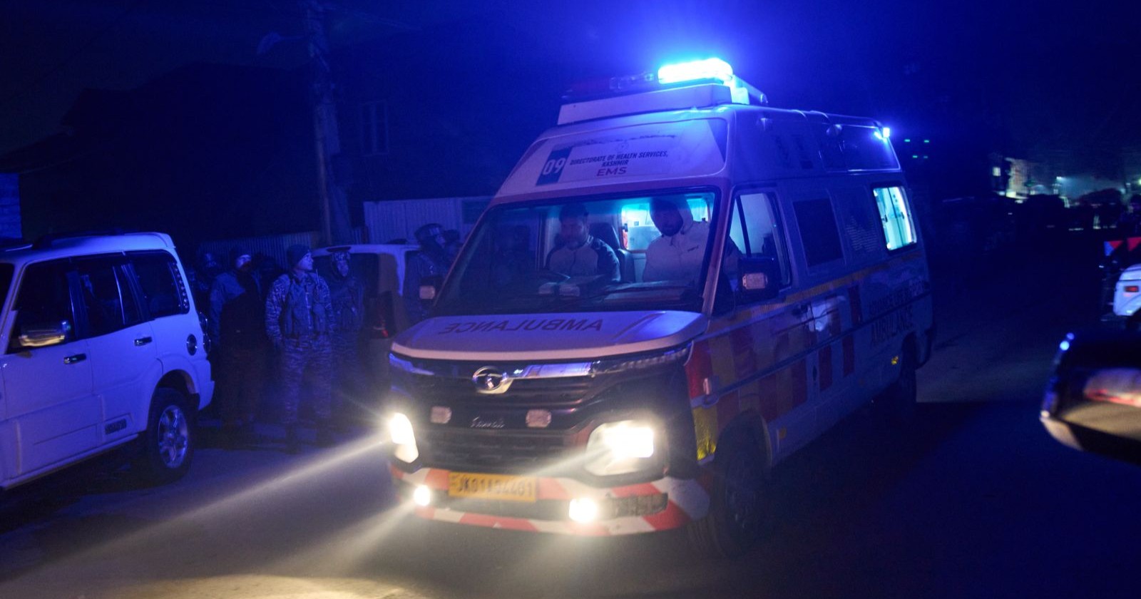 Ambulanzfahrzeug mit eingeschaltetem Blaulicht in einer dunklen Straße in Amritsar, umgeben von Einsatzkräften und Fahrzeugen.