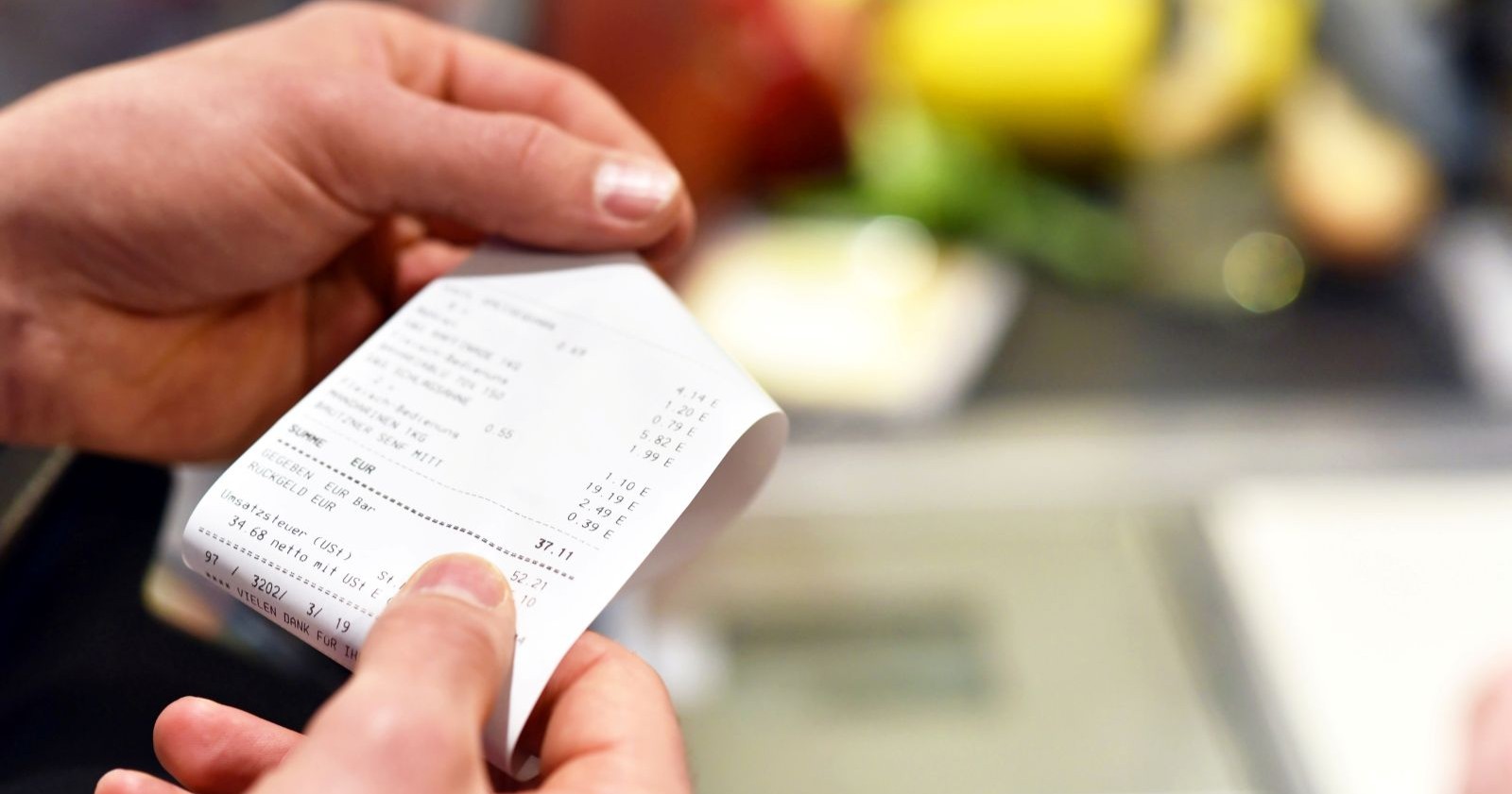 Mann hält nach einem Einkauf im Supermarkt eine Rechnung in seinen Händen