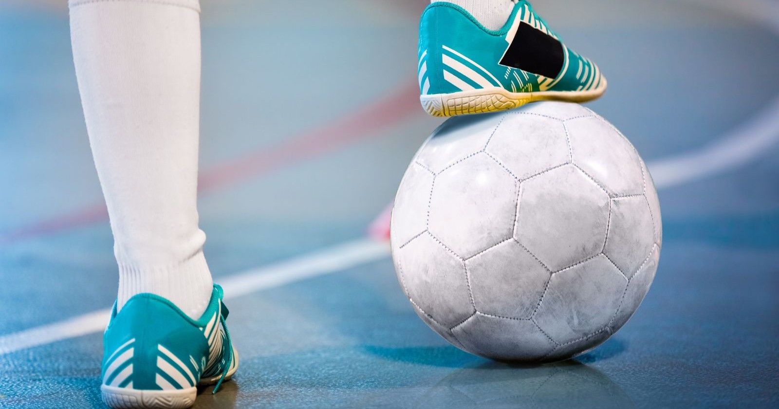 Fußballer der mit Hallenschuhen auf einem weißen Ball in einer Turnhalle steht