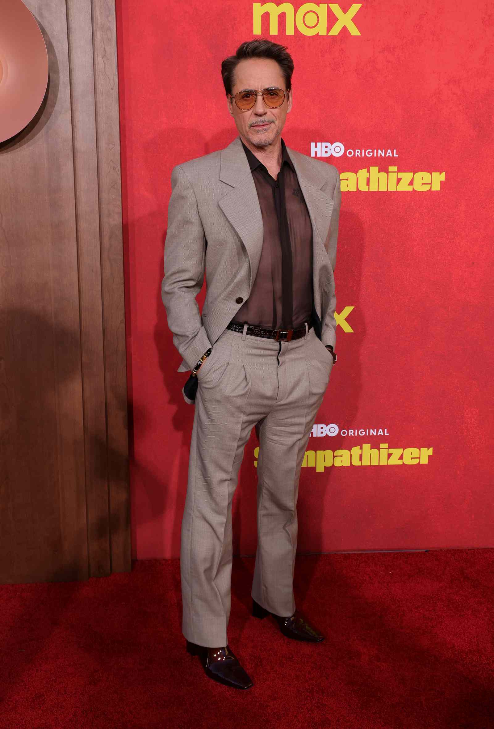 Robert Downey Jr. posiert auf dem roten Teppich vor einer roten „HBO Original“-Fotowand und trägt einen hellen Anzug mit Sonnenbrille.
