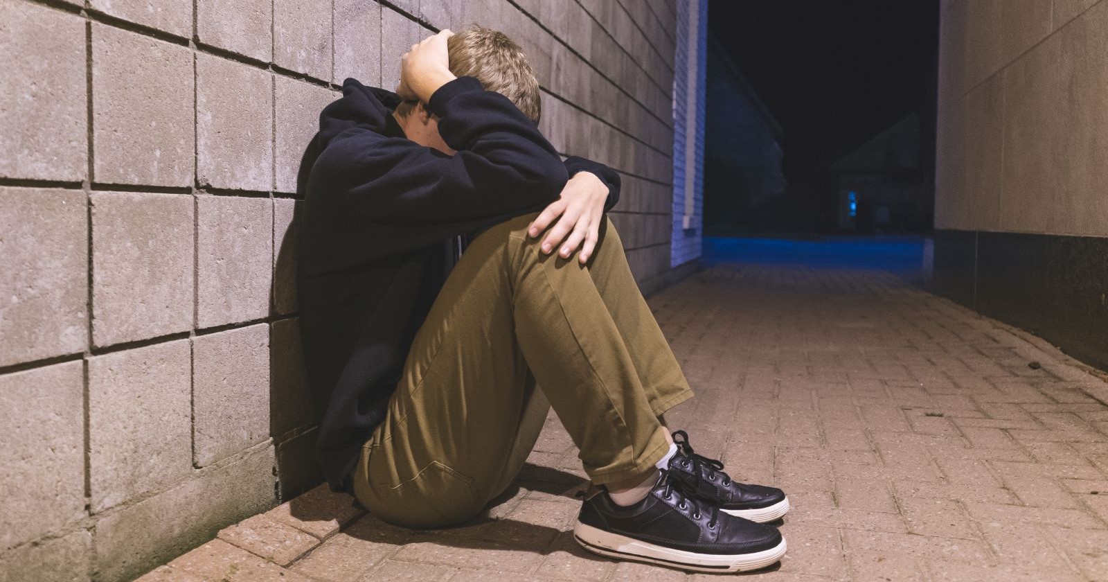 Kind sitzt zusammengekauert auf Boden