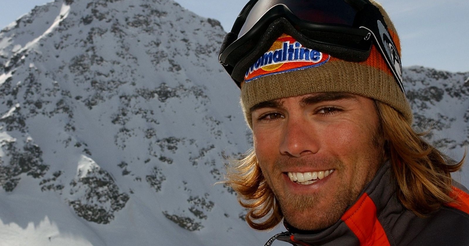 Snowboarder Ueli Kestenholz mit Mütze und Skibrille lachend vor einem schneebedeckten Berg. Eine Lawine hat ihn das Leben gekostet.