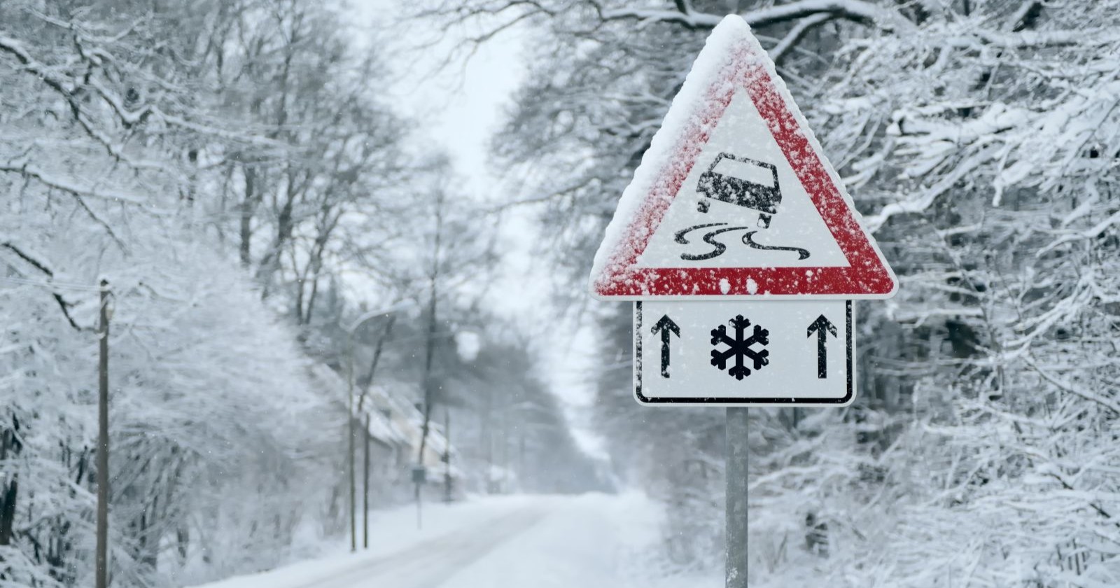 Verschneite Straße mit Warnschildern von Rutschgefahr für Autos