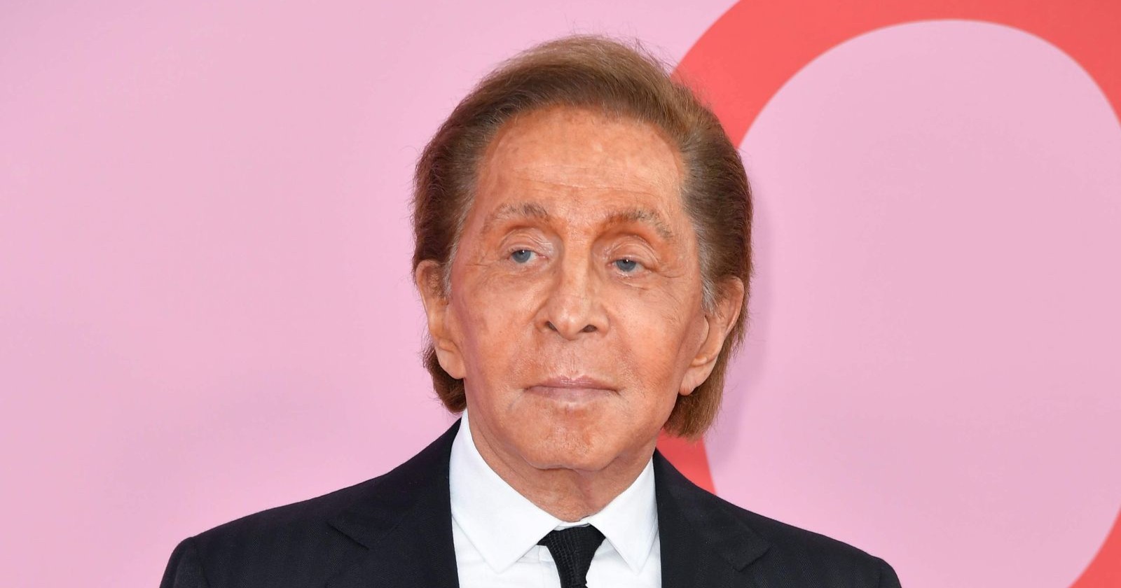 Porträt des italienischen Modedesigners Valentino Garavani in schwarzem Anzug und Krawatte vor rosafarbenem Hintergrund. Der Designer ist im Alter von 93 Jahren verstorben.