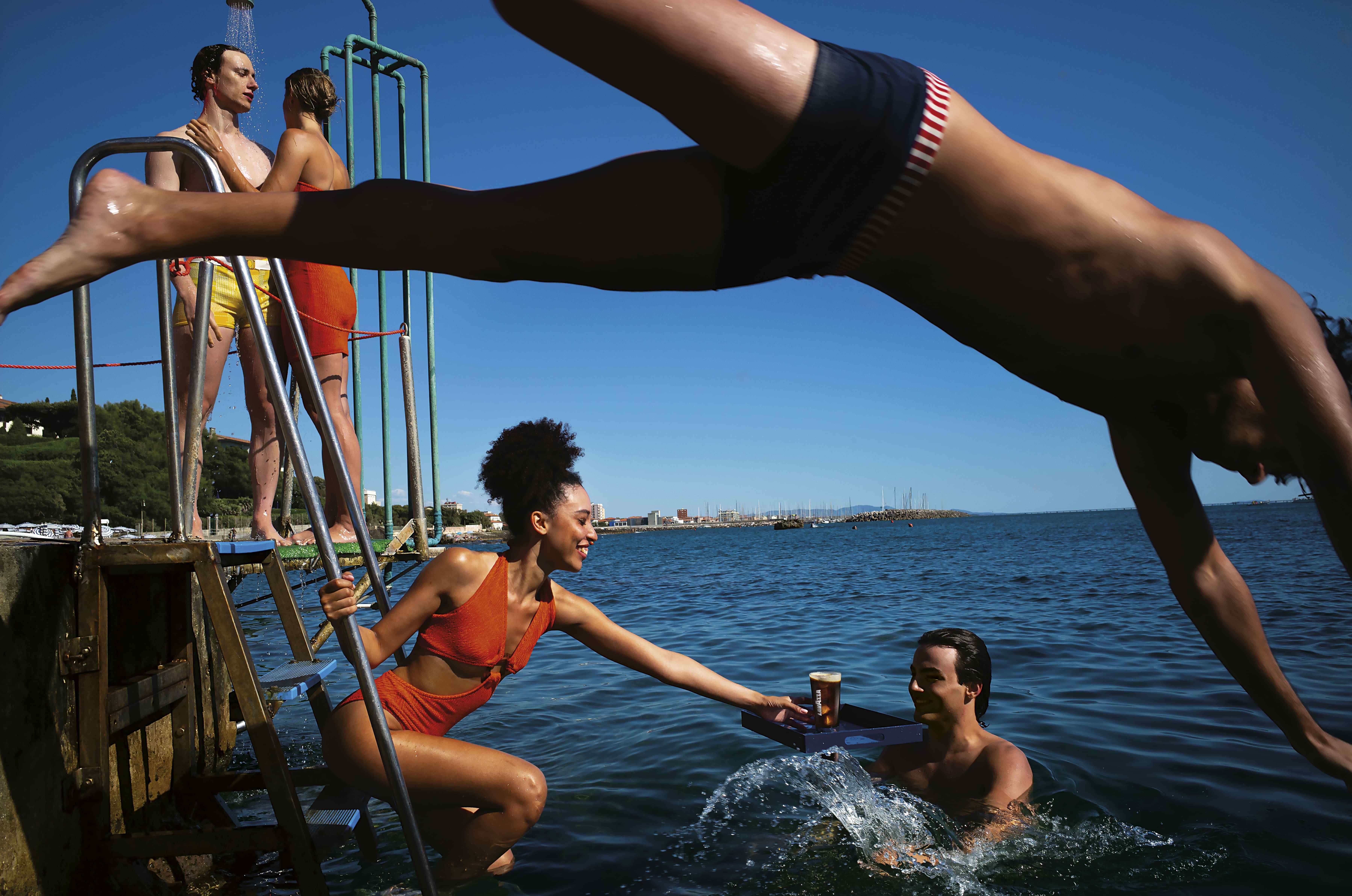Szene am Meer mit mehreren badenden und hineinspringenden Menschen