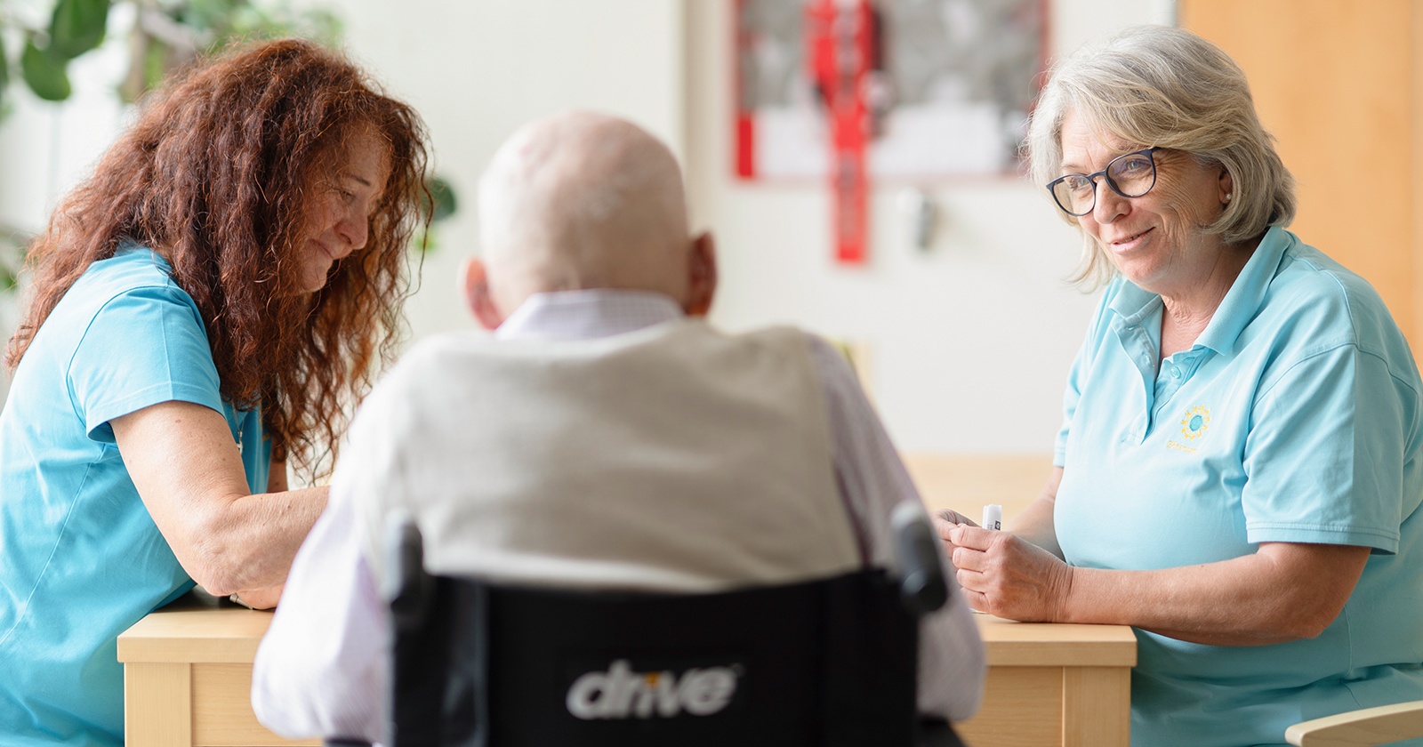 Pflegerinnen im Gespräch mit einem alten Mann im Rollstuhl | Credit: Krankenhaus der Barmherzigen Brüder