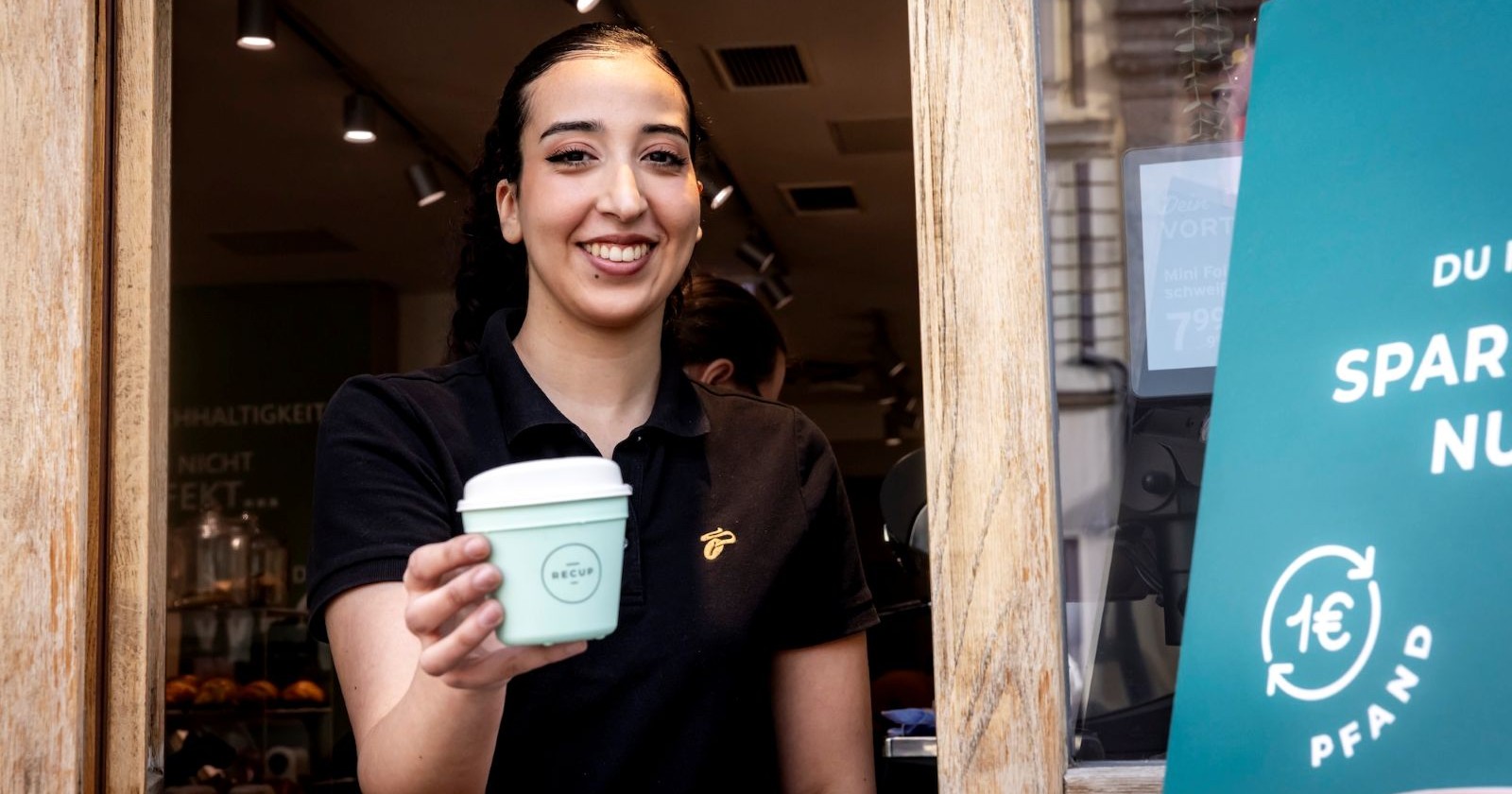 Junge Frau schauit aus Fenster und hält Mehrwegtasse
