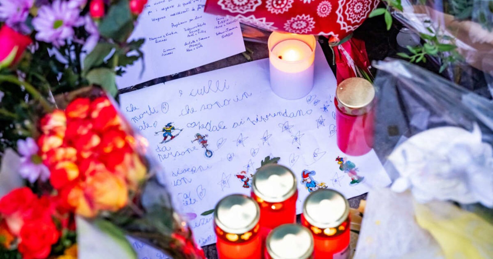 Kerzen, Blumen und Briefe liegen auf einer Straße.