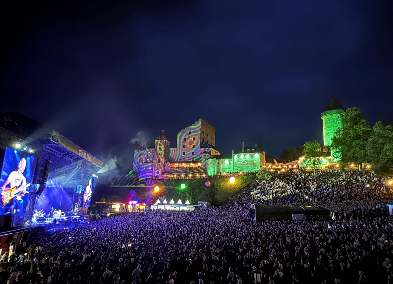 Großes Open-Air-Konzert vor der beleuchteten Burg Clam bei Nacht mit Bühne und dichtem Publikum.