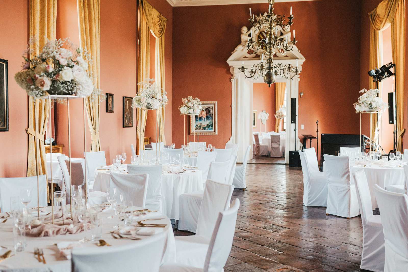 Festlich gedeckter Saal in Burg Rabenstein mit weißen Tischen, hohen goldenen Vorhängen, Kronleuchter und historischen Details.