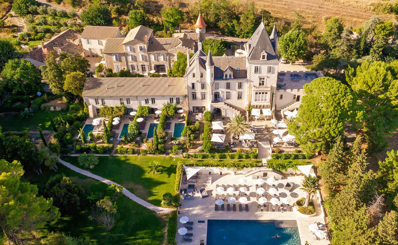 Luftaufnahme von Château Les Carrasses in Südfrankreich mit Pool, Parkanlage und Weinbergen in der Umgebung.