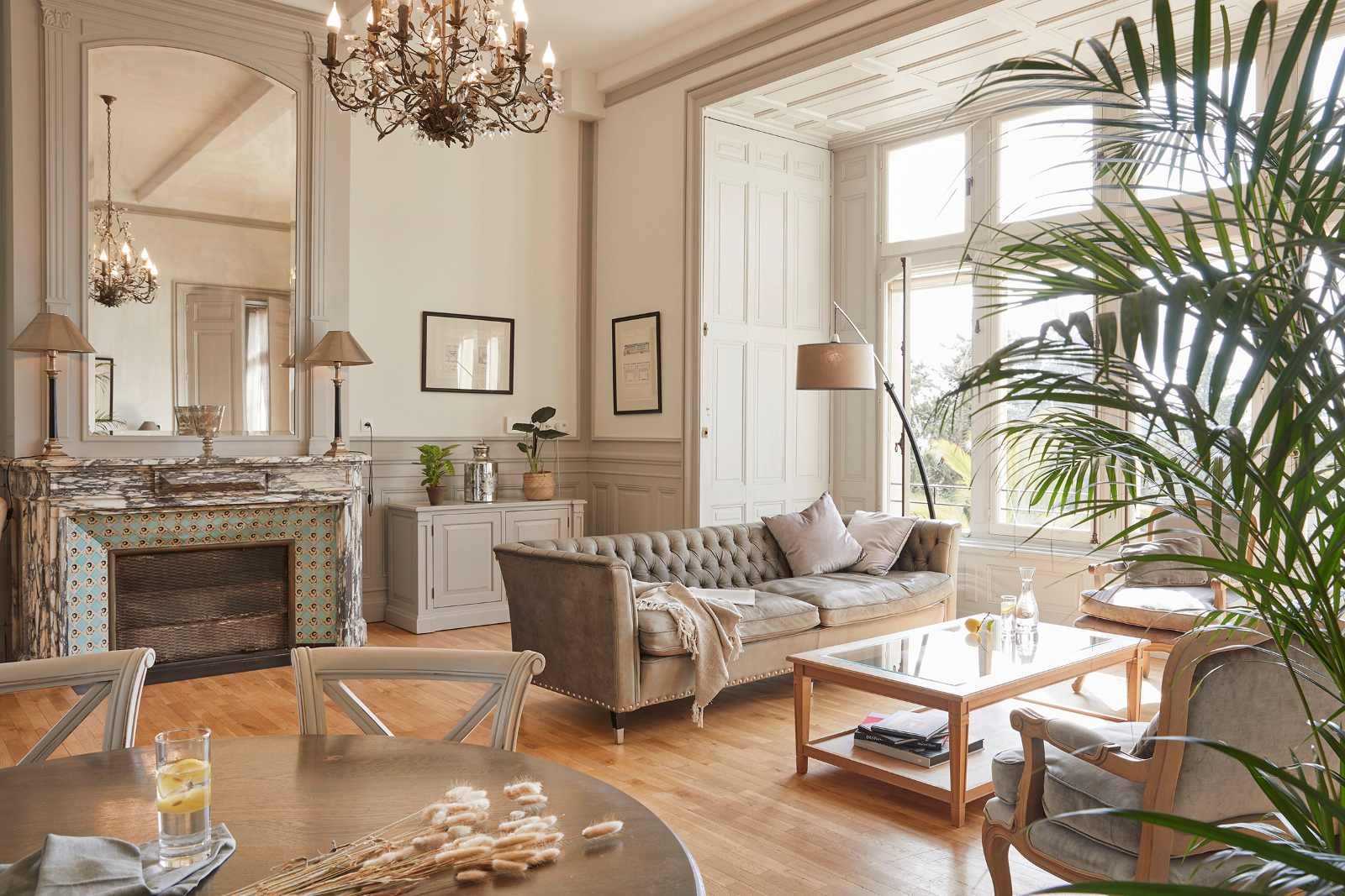 Eleganter Salon im Château Les Carrasses mit Kronleuchter, Kamin, hohen Fenstern und klassischer Einrichtung.  Titel