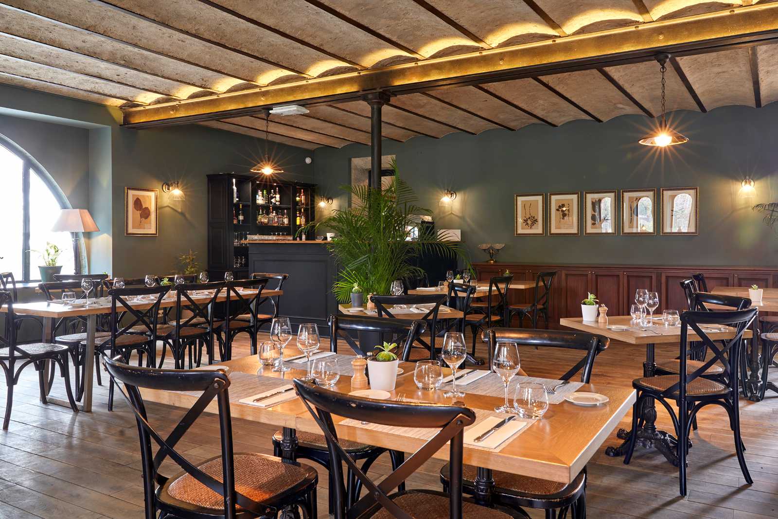 Stilvoll eingerichtetes Restaurant im Château Les Carrasses mit Holztischen, Barbereich und warmem Licht.