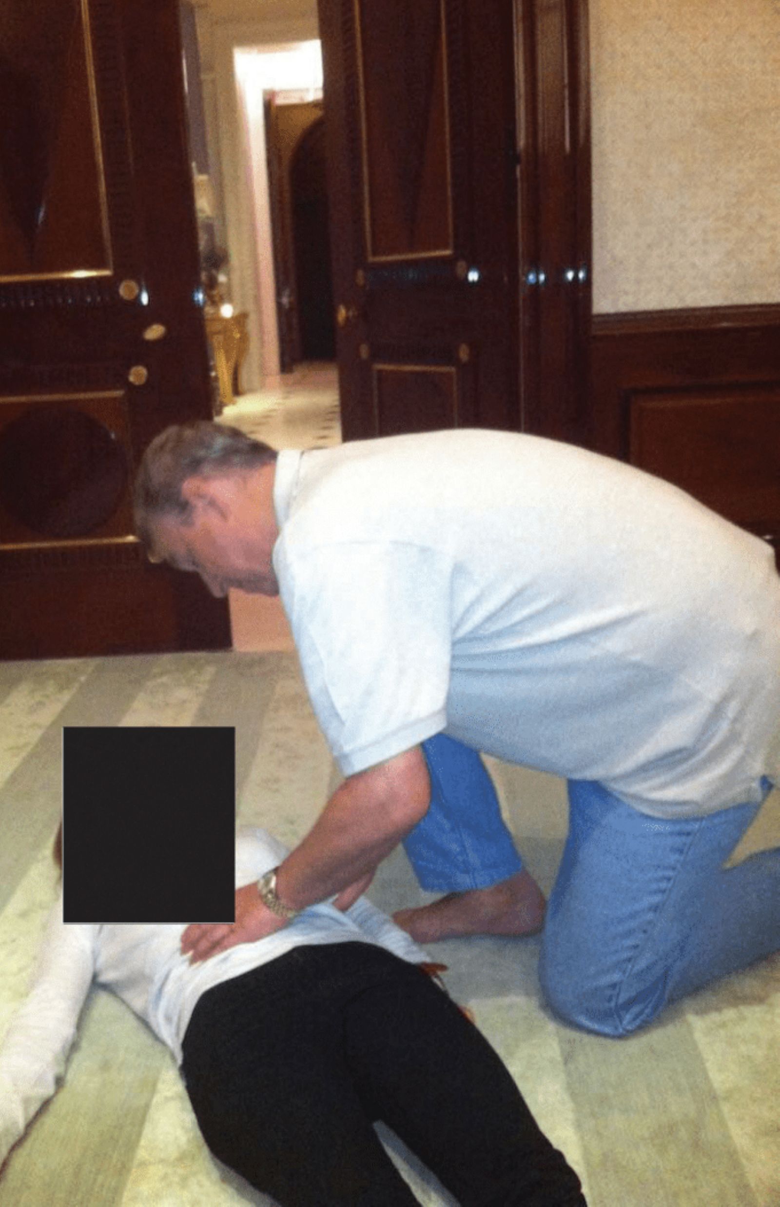 Ein Mann kniet barfuß in einem prunkvollen Raum über einer am Boden liegenden Frau mit geschwärztem Gesicht.