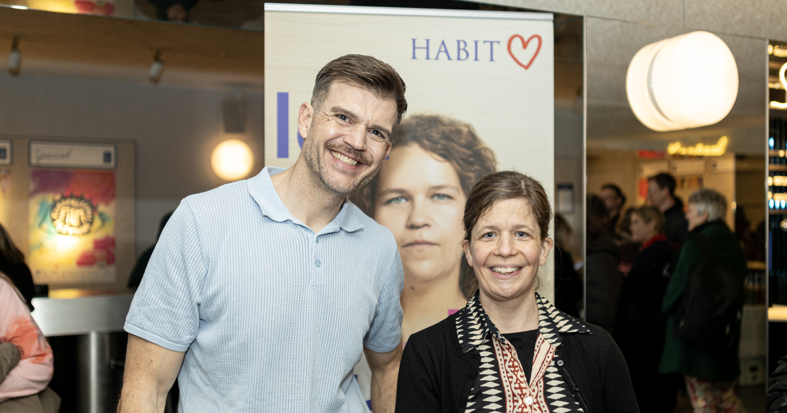 Mann und Frau im Stadtkino vor einem Aufsteller des Hauses der Barmherzigkeit