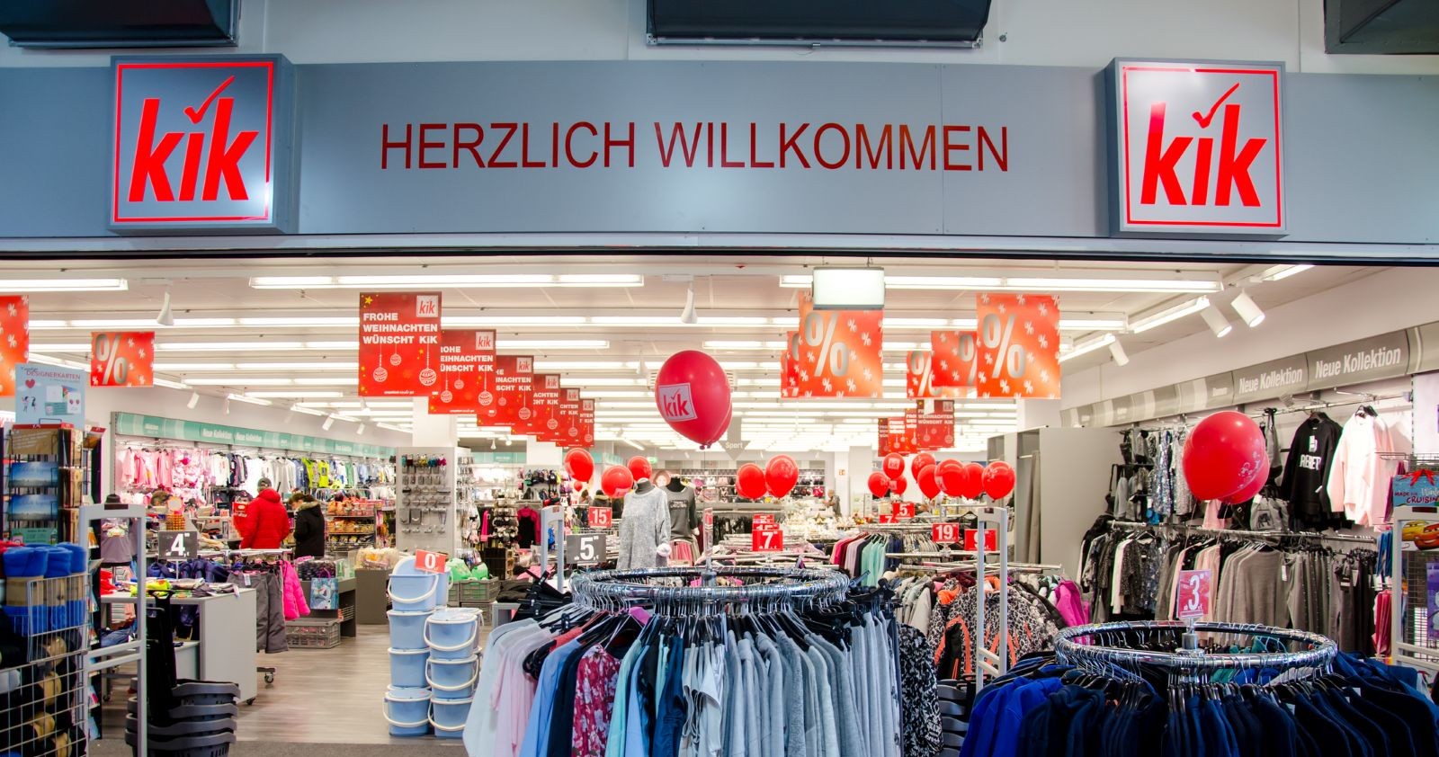 Innenansicht einer KiK-Filiale mit Kleiderständern, roten Rabatt-Schildern und KiK-Logo über dem Eingang – Kik schließt auch in Österreich Filialen