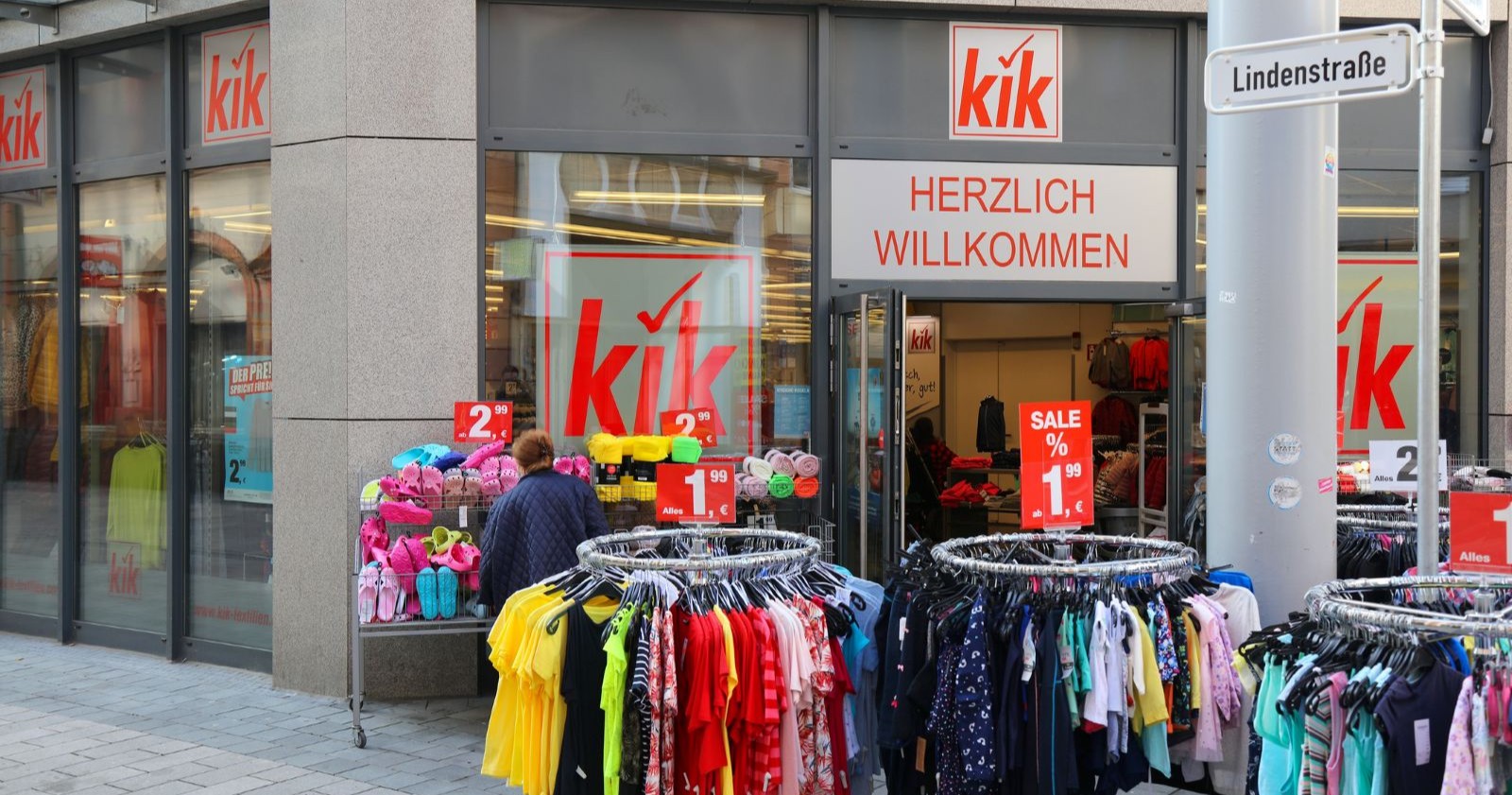 Eingang einer KiK-Filiale mit Kleiderständern und SALE-Schildern vor dem Geschäft.