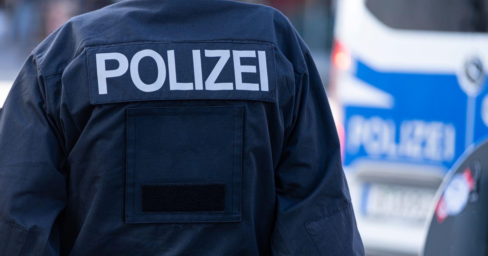Rückansicht eines Polizisten vor einem Einsatzfahrzeug – Symbolbild für laufende Ermittlungen der Polizei in Kitzbühel.