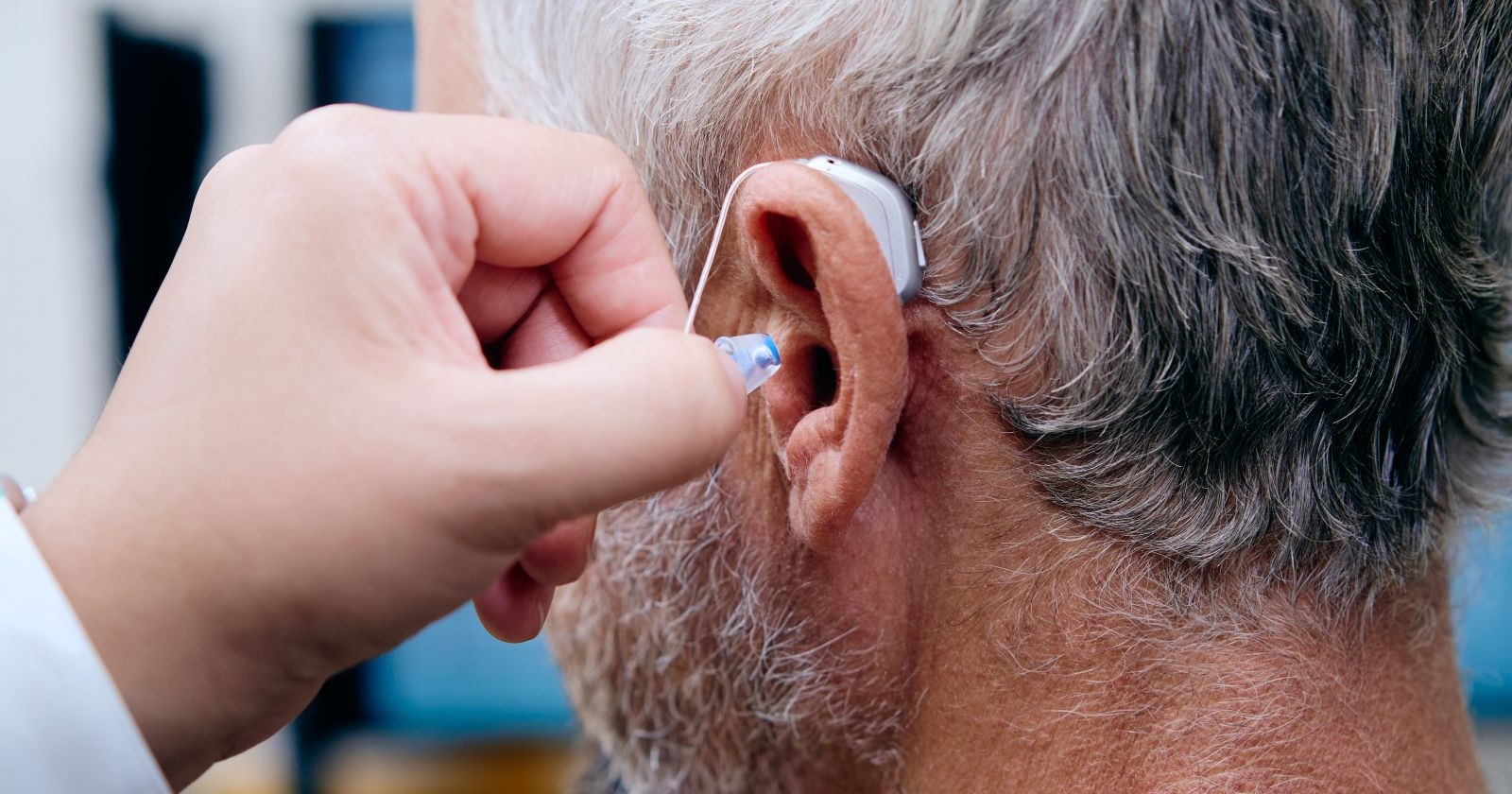 Akustiker steckt Hörgerät in das Ohr eines Mannes mit grauen Haaren
