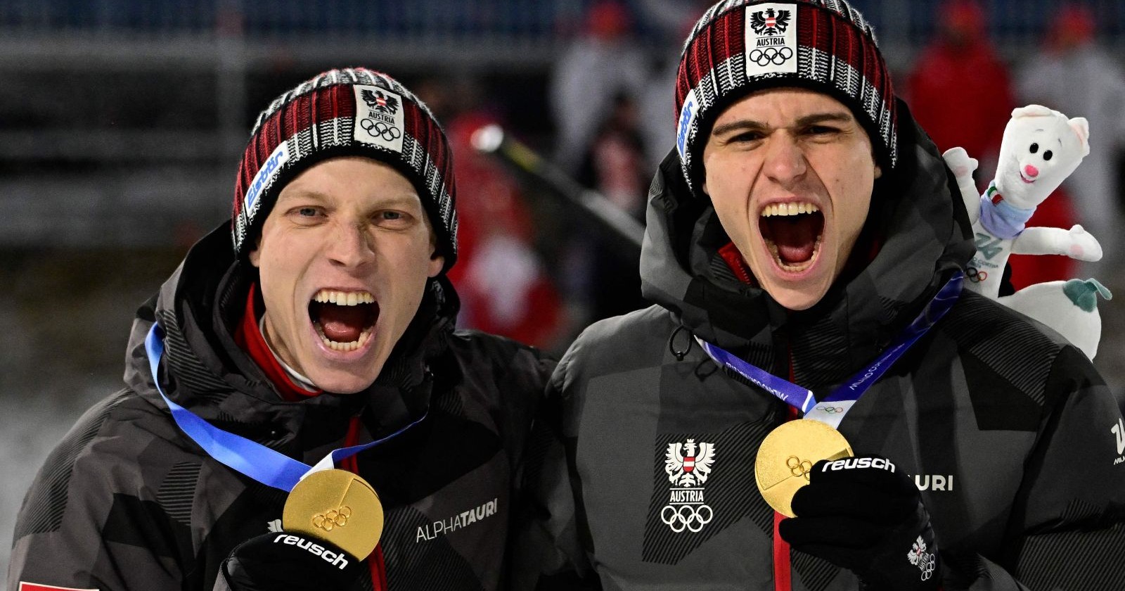 Jan Hörl und Stefan Embacher Teamjacken mit Olympia-Logo halten ihre Goldmedaillen hoch und jubeln nach dem Sieg im Super-Team-Bewerb der Winterspiele 2026.