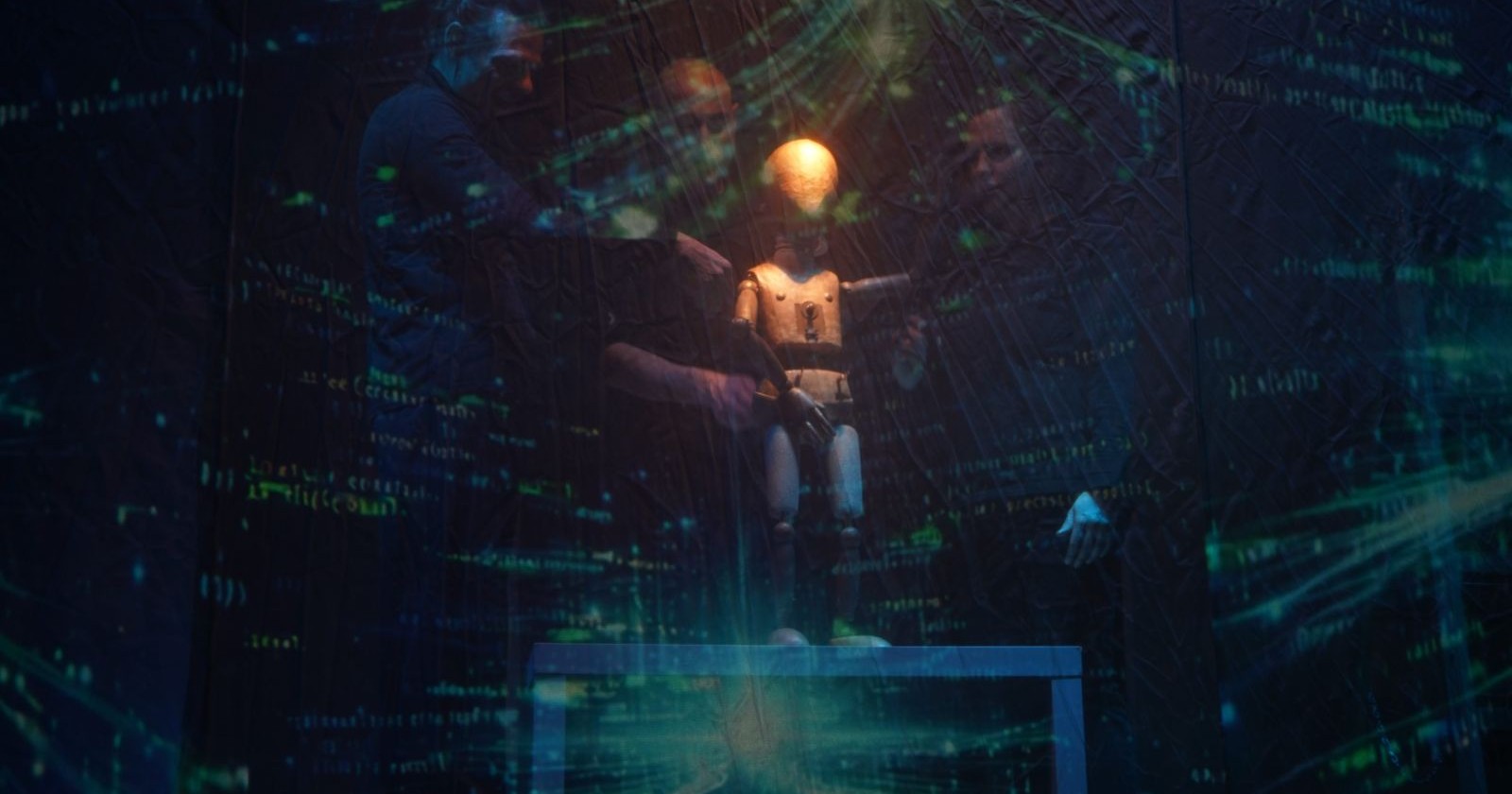 Drei Schauspieler mit einer Holzpuppe in einem grün-gedimmten Licht