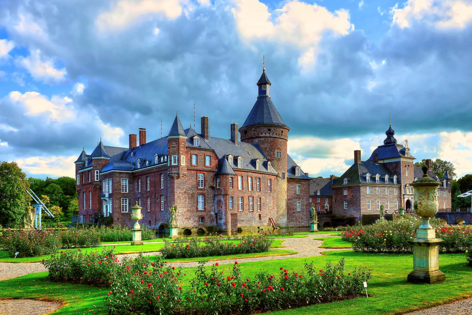 Wasserburg Anholt in Nordrhein-Westfalen mit roten Backsteinfassaden, runden Türmen und gepflegter Gartenanlage im Vordergrund.