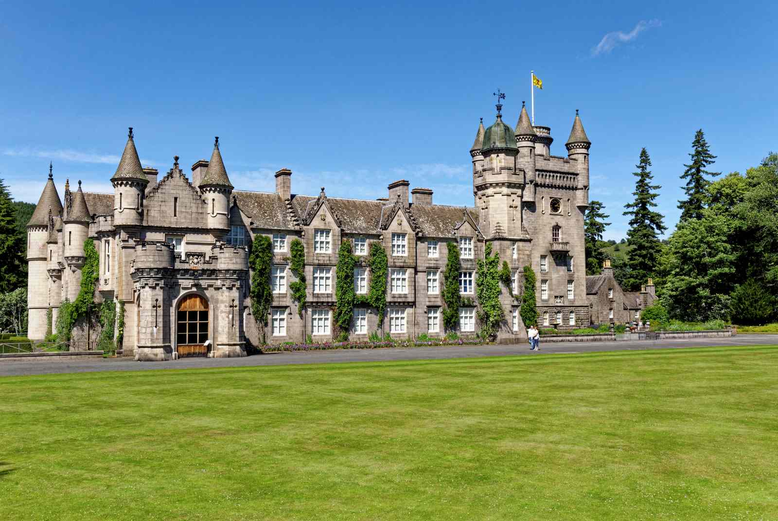 Balmoral Castle in Schottland mit Türmen und grauer Steinfassade, umgeben von gepflegtem Rasen und Bäumen.